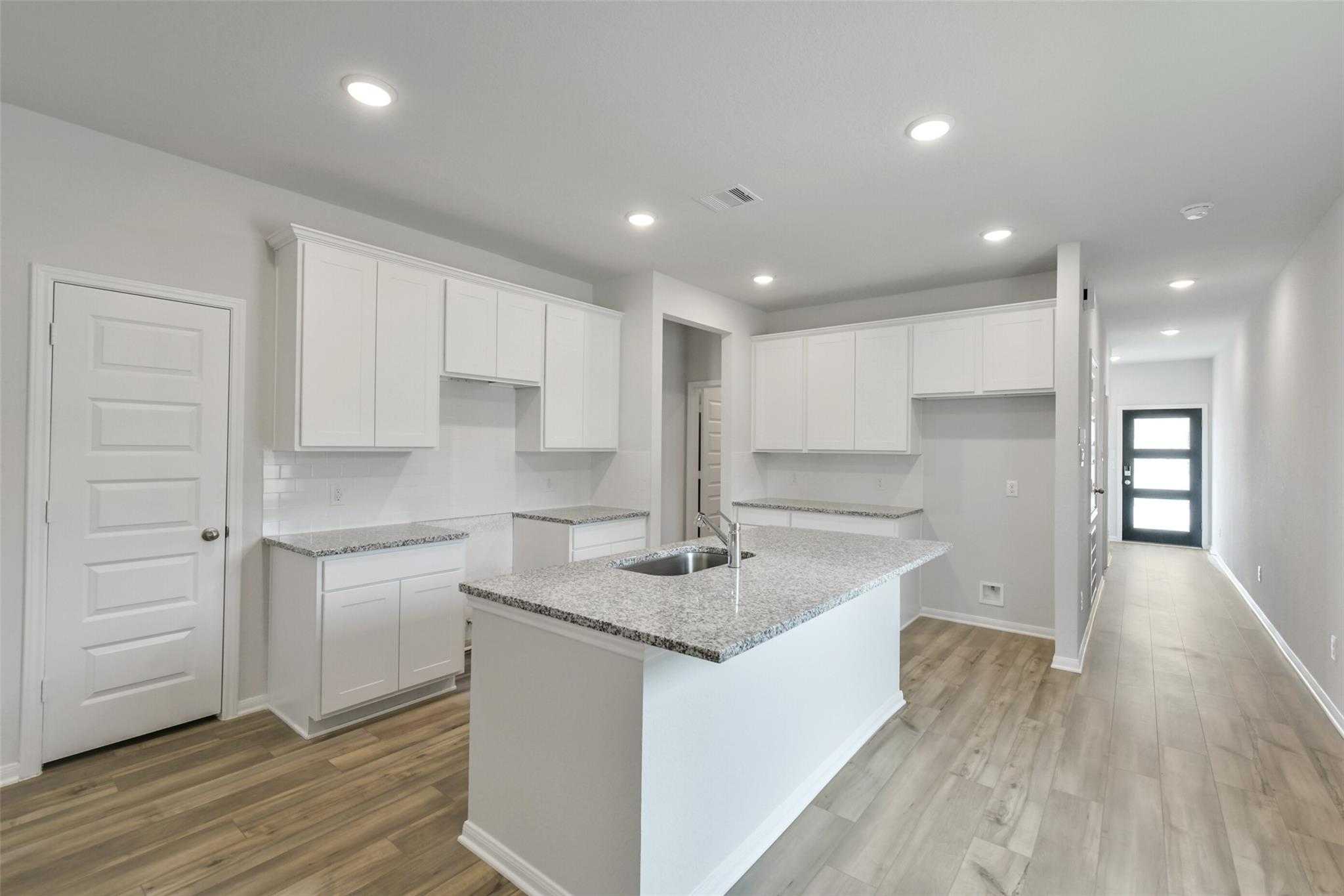Modern white kitchen with granite island sink, shaker cabinets, and open layout in Davidson Homes The Frio G, Conroe, Texas