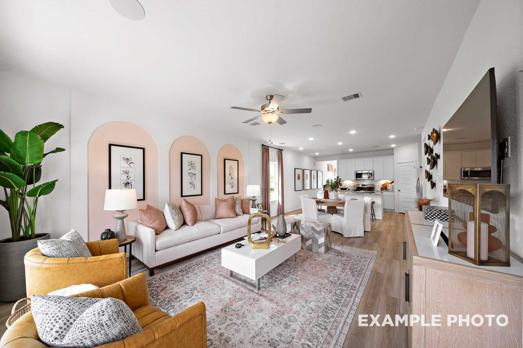 Open-concept living room in The Sabine E showcasing white sofa, orange armchairs, pink rug, arched walls, and adjacent kitchen