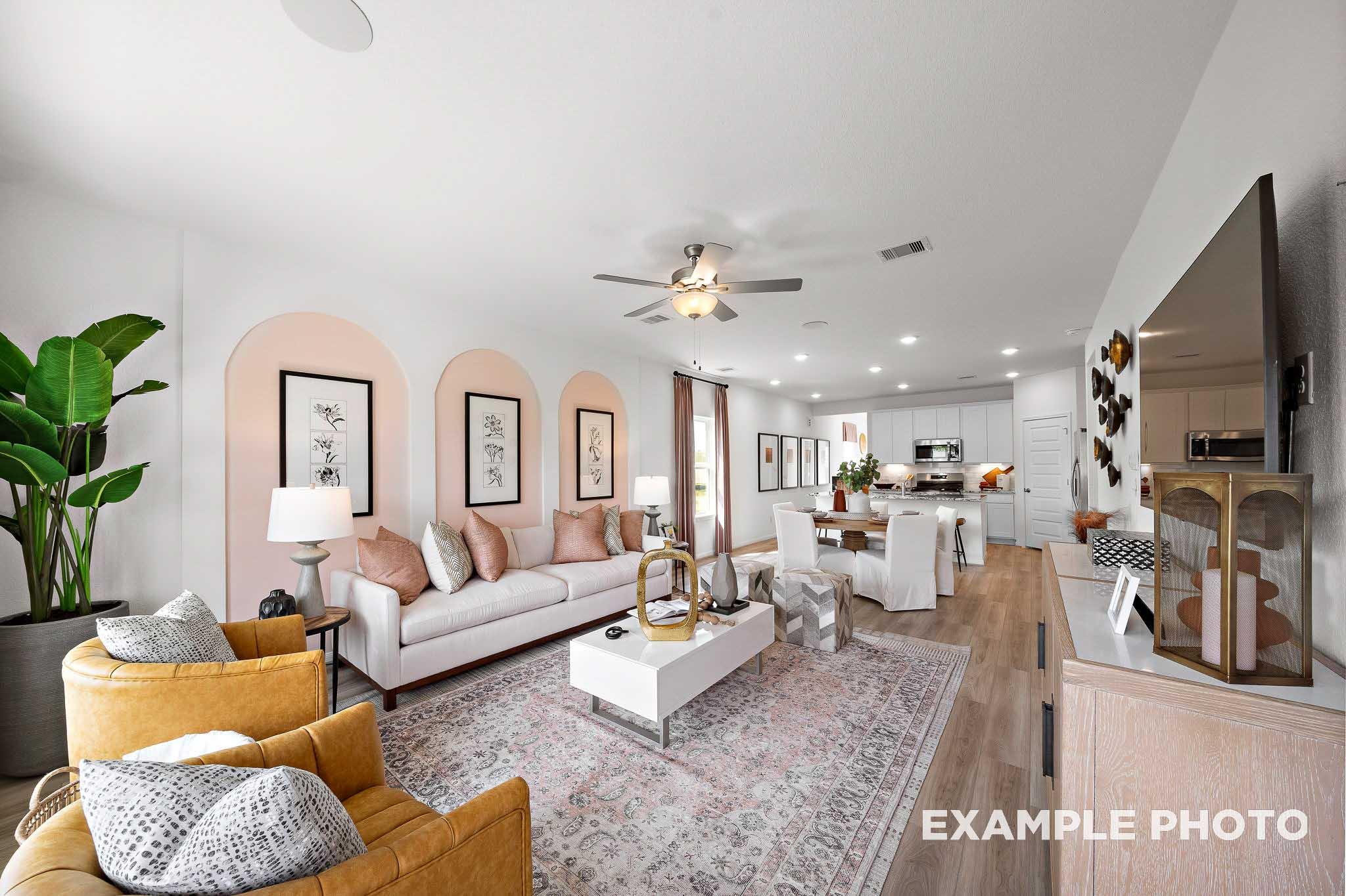 Open-concept living room in The Sabine E showcasing white sofa, orange armchairs, pink rug, arched walls, and adjacent kitchen