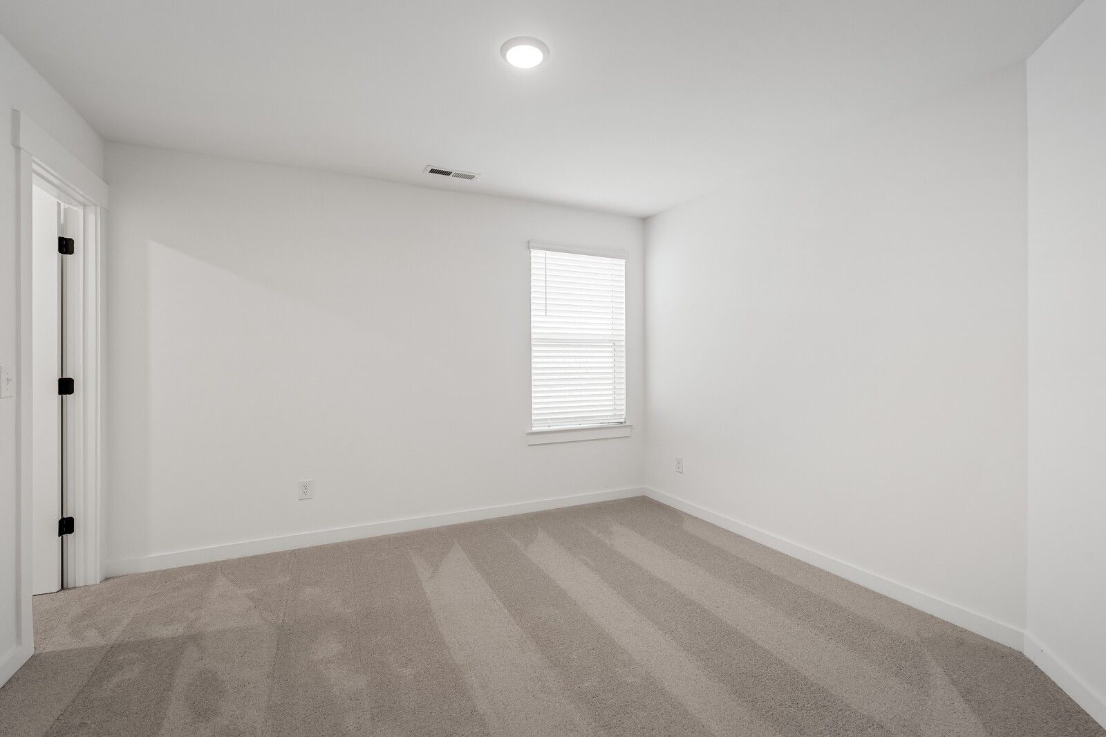 Bright empty bedroom with white walls, beige carpet, and window blinds in Davidson Homes The Ridgeport, Gallatin, Tennessee