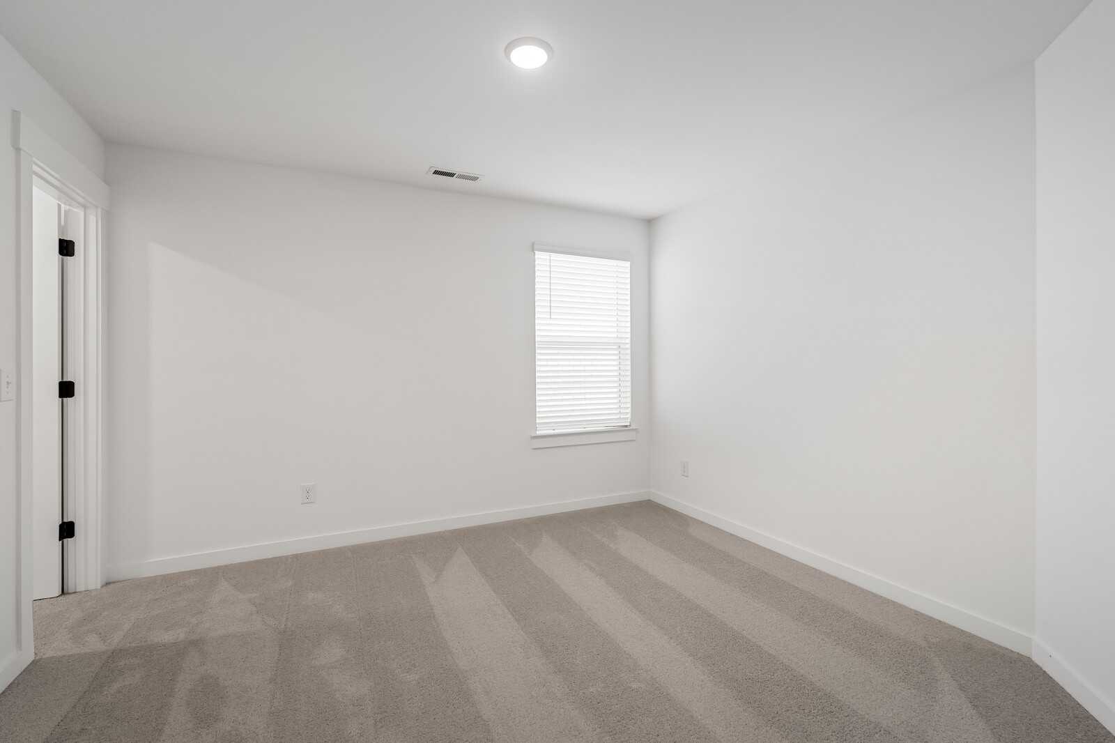 Bright empty bedroom with white walls, beige carpet, and window blinds in Davidson Homes The Ridgeport, Gallatin, Tennessee