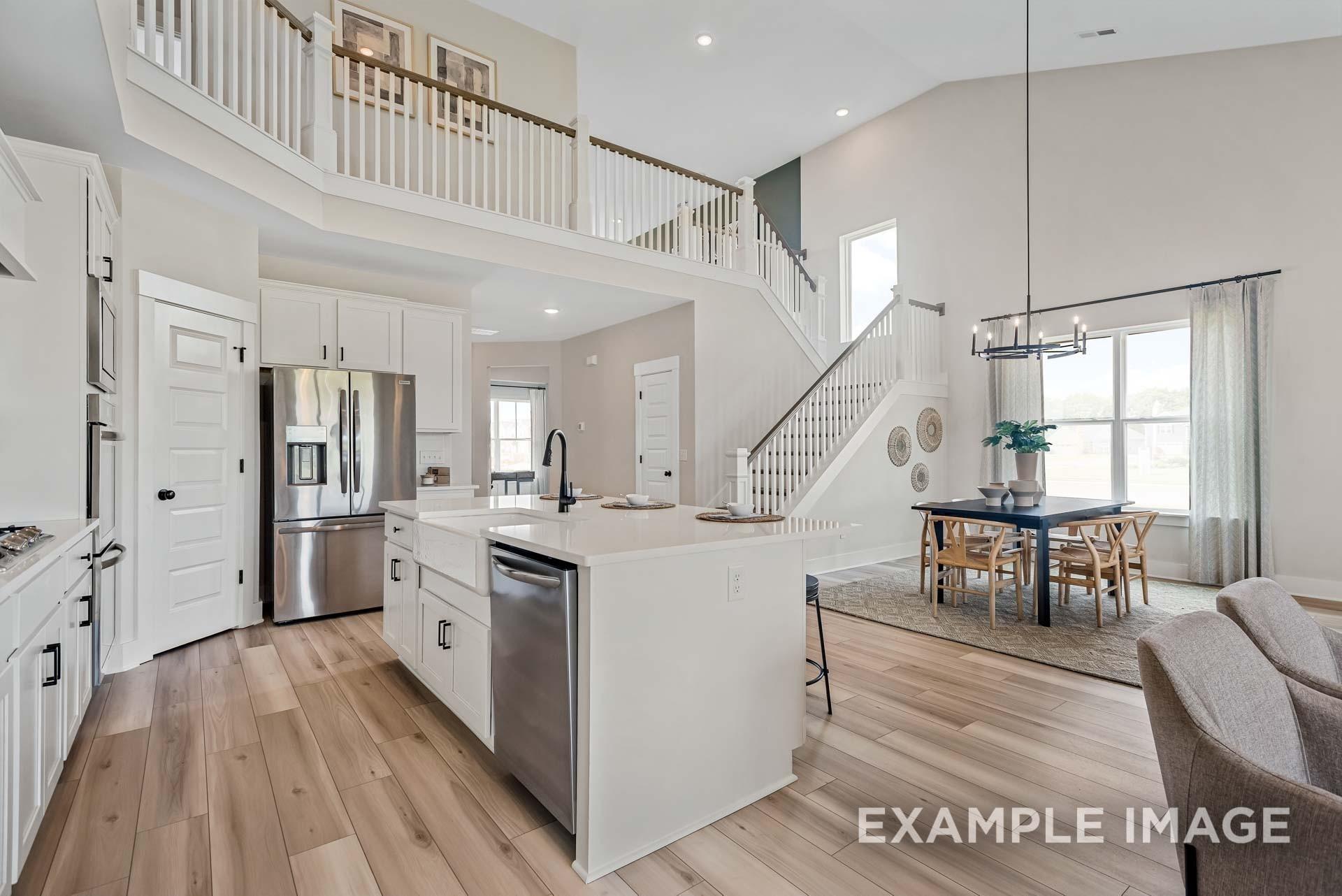 Open-concept kitchen with white cabinets, stainless appliances, island sink, adjacent dining area, and two-story staircase in The Ridgeport home, Gallatin, TN