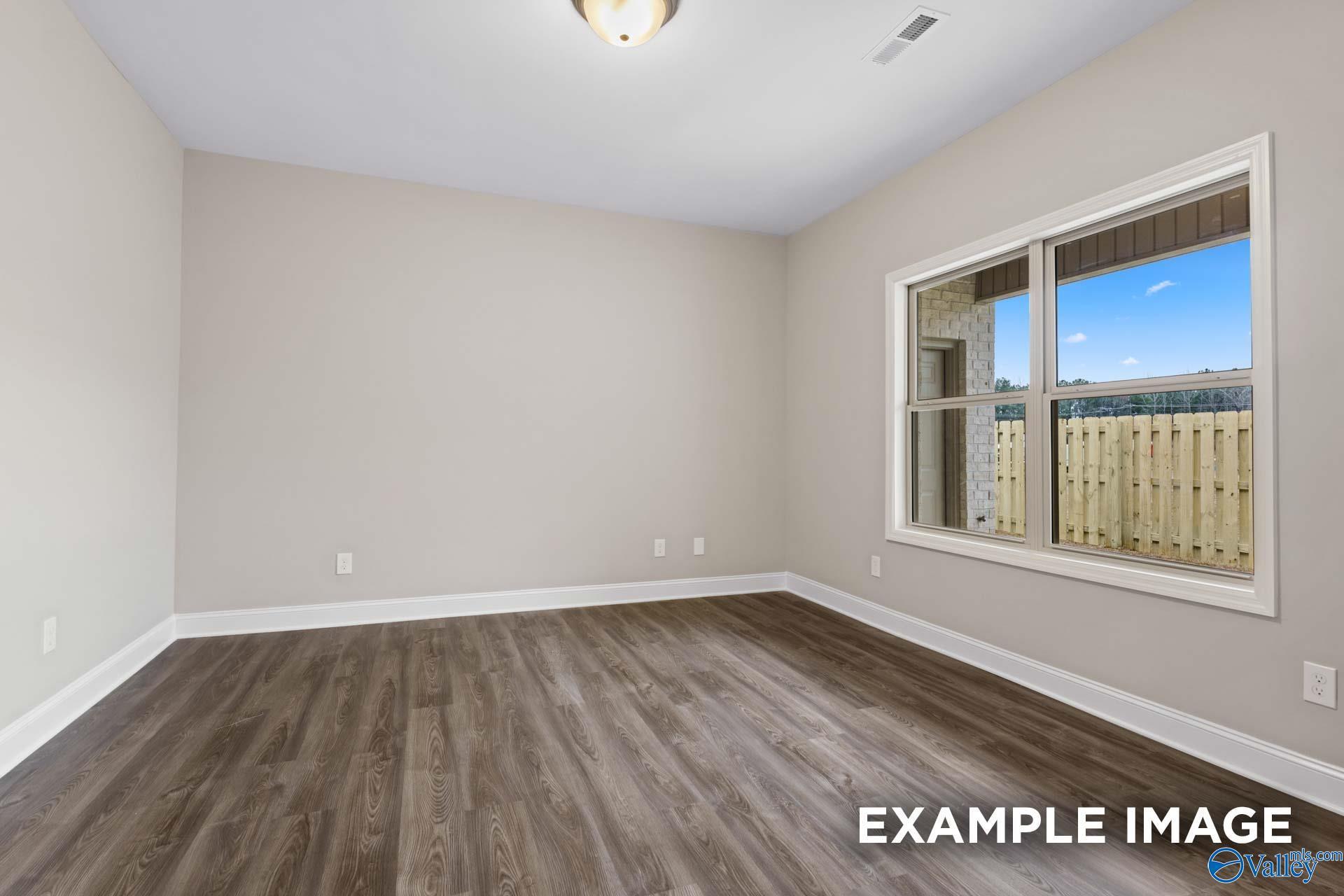 Empty bedroom with hardwood floors, beige walls, and large window overlooking fenced backyard in Davidson Homes The Camilla A, Hartselle, AL