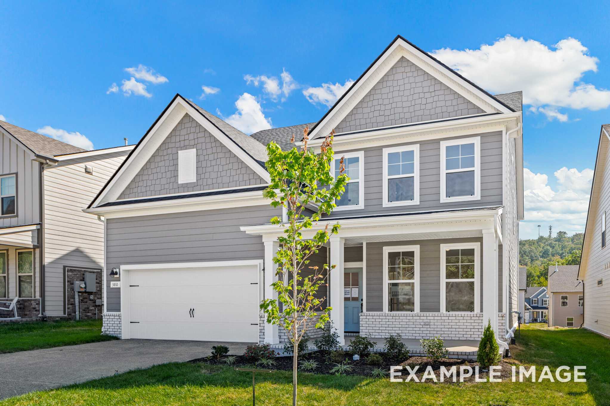 Two-story gray craftsman elevation of The Henry C by Davidson Homes, with gabled roof, front porch, two-car garage, and young tree in Mt. Juliet, TN