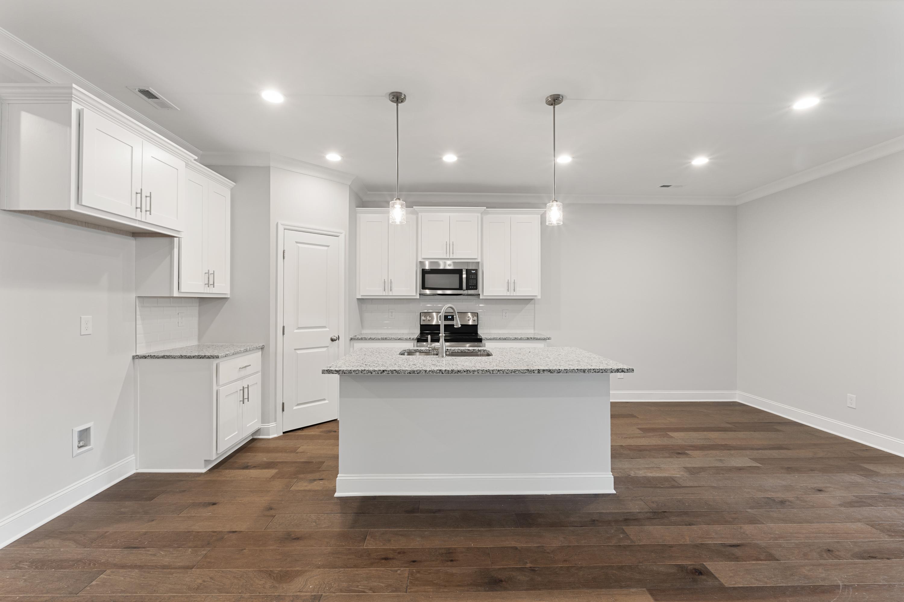 Bright modern kitchen in The Copeland C by Davidson Homes, Madison AL, with white cabinets, large island, stainless sink, and hardwood floors