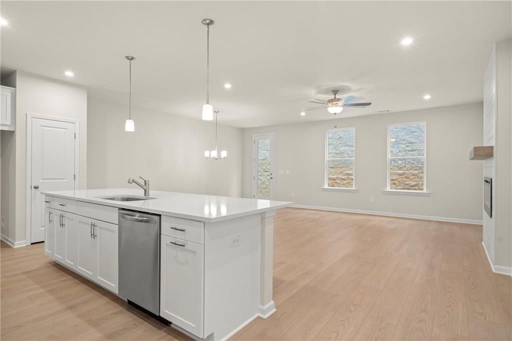 Modern open-concept kitchen with white island, stainless dishwasher, pendant lights, and hardwood floors in The Cary A, Kennesaw, GA