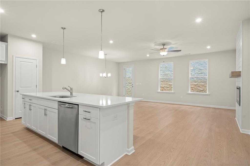 Open-concept kitchen with white island, stainless dishwasher, pendant lights, and large windows in Davidson Homes The Cary A, Kennesaw, GA
