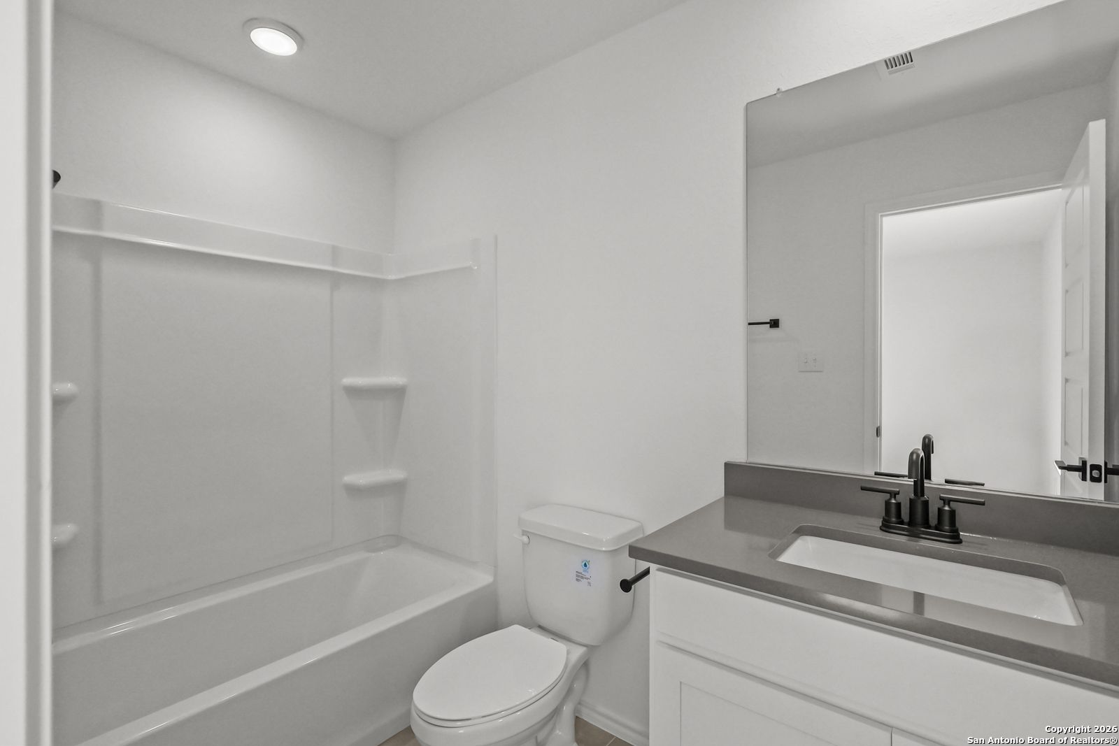Bright white guest bathroom with tub-shower combo, granite vanity, and mirror in Davidson Homes The Douglas E, San Antonio