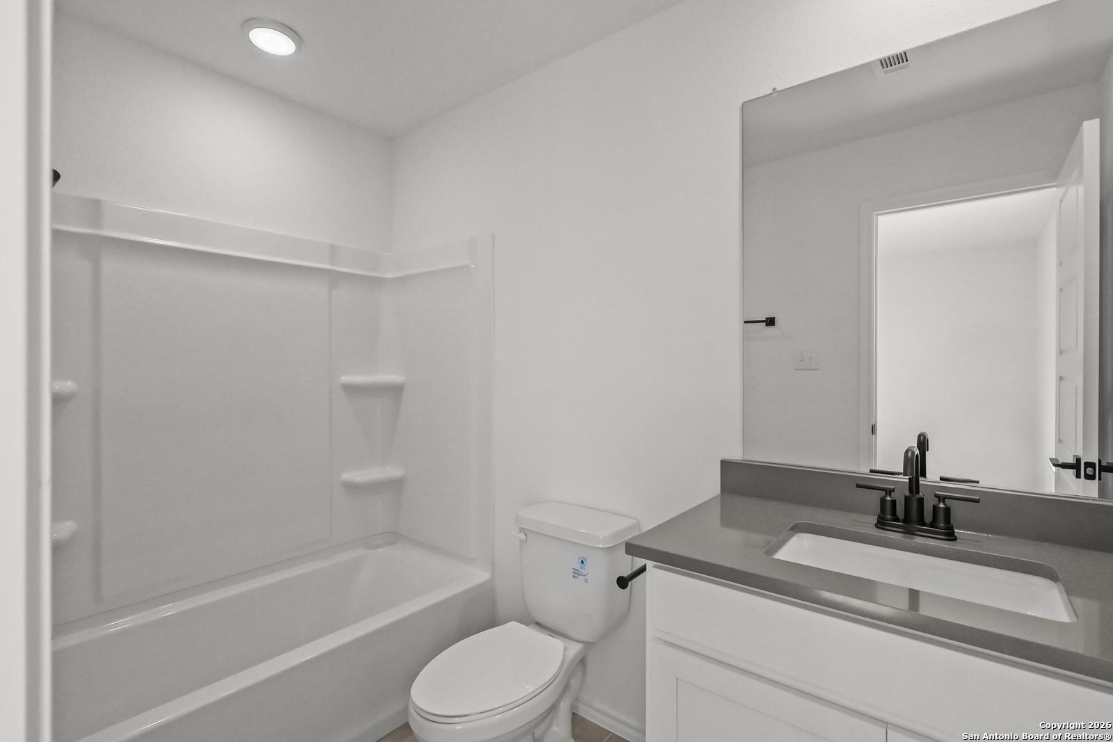 Bright white guest bathroom with tub-shower combo, granite vanity, and mirror in Davidson Homes The Douglas E, San Antonio