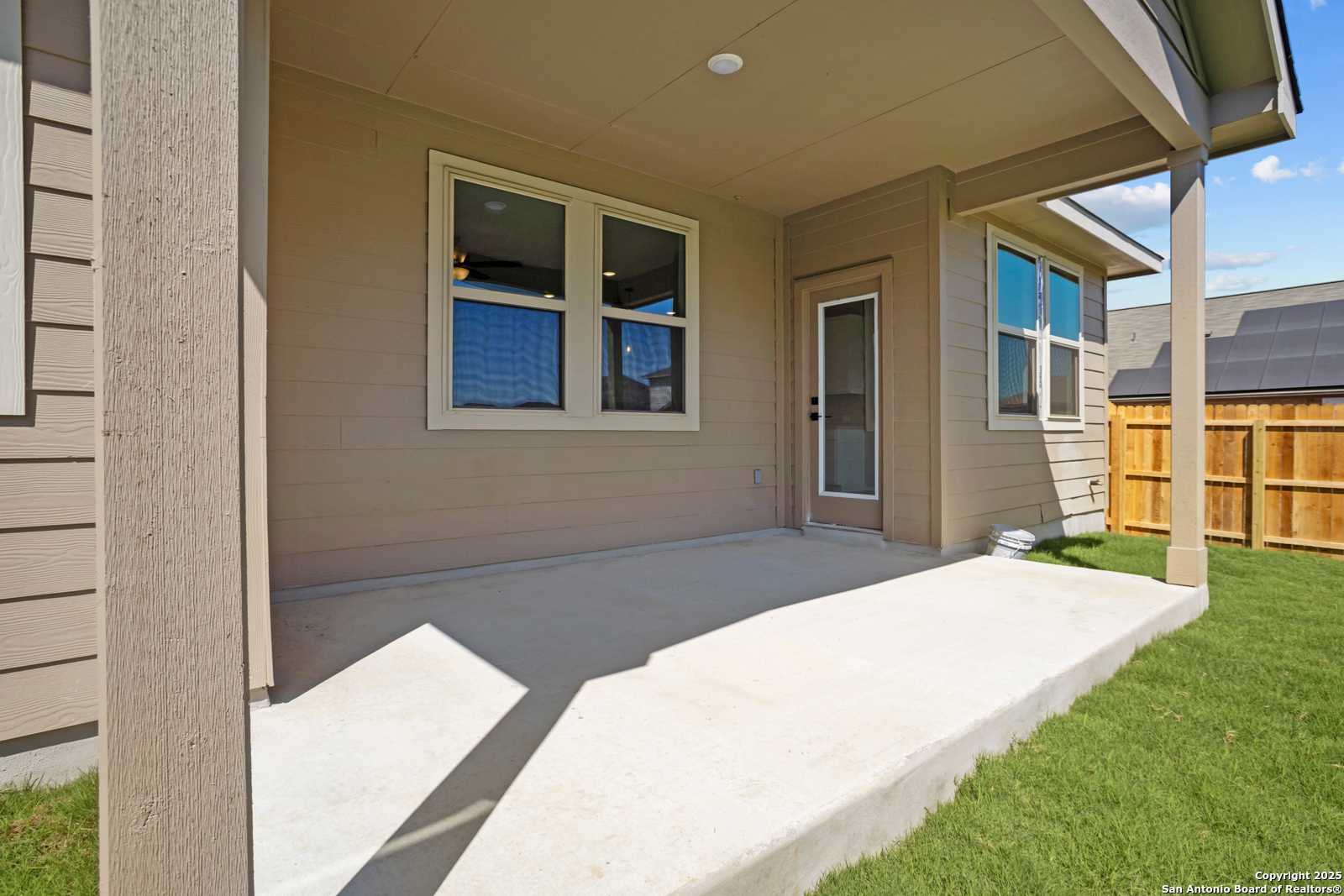 Covered back patio with beige siding, large windows, and wooden fence in Davidson Homes The Asheville E, Converse, Texas