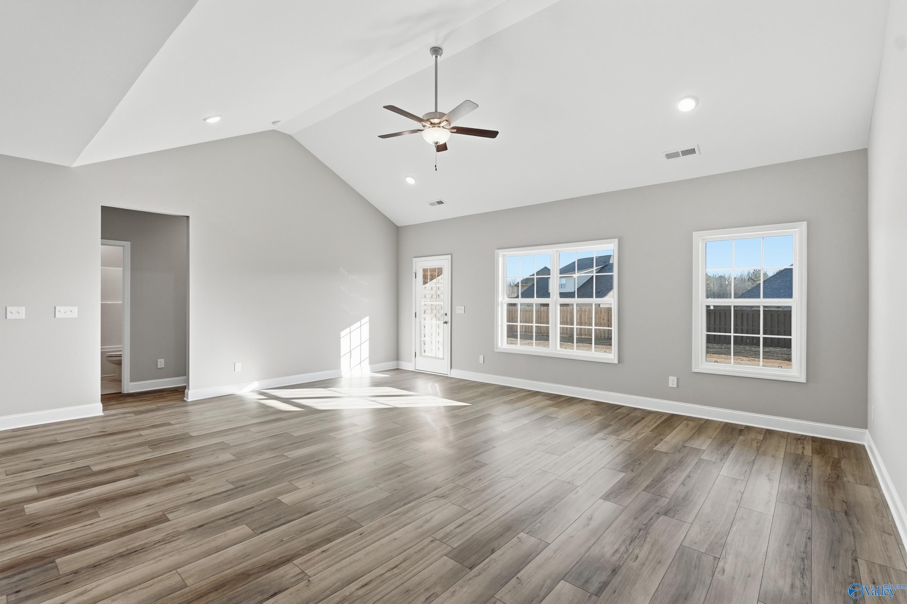 Bright living room with vaulted ceiling, ceiling fan, large windows, and luxury flooring in Davidson Homes The Lanier, Toney, Alabama