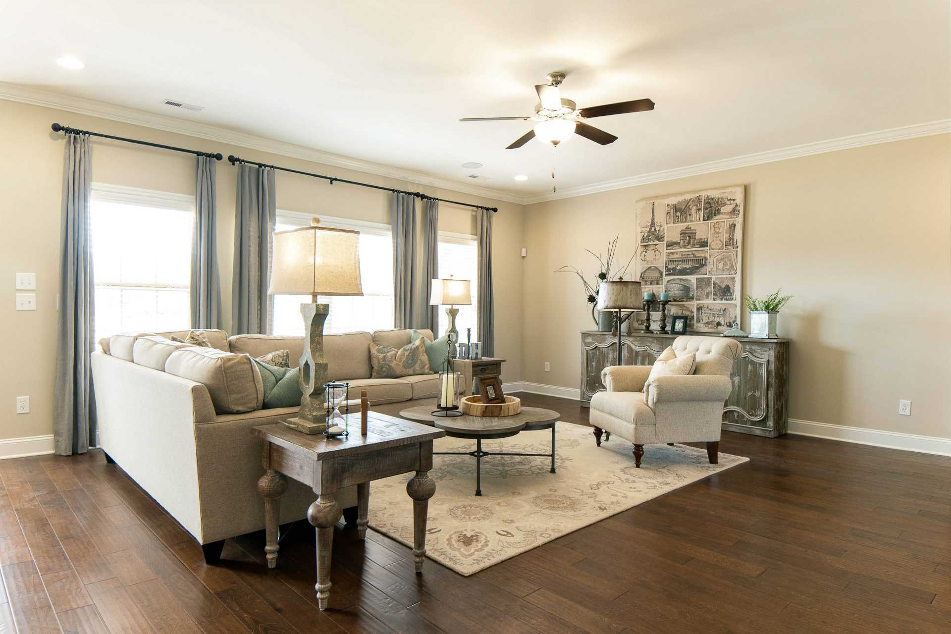 Open-concept living room at The Dairy at Oak Grove in South Huntsville AL featuring beige sectional sofa, hardwood floors, large windows, and ceiling fan