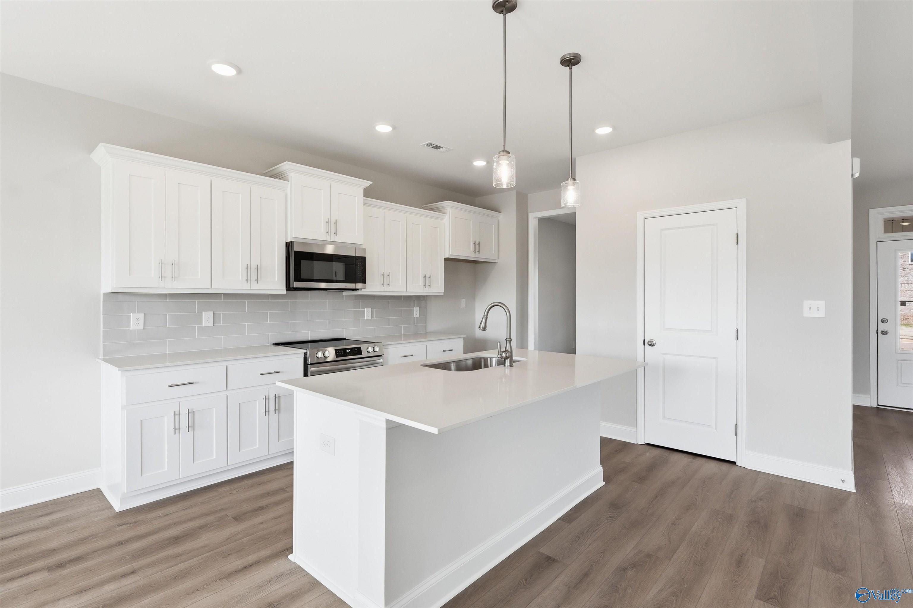 Modern kitchen with white cabinets, quartz island, and stainless appliances in The Shelby D home, Evergreen Mill, Madison.