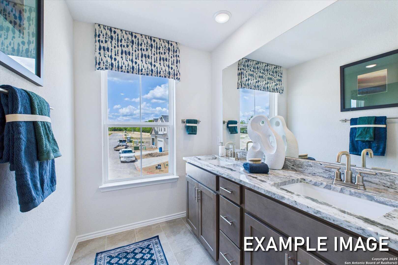 Elegant master bathroom featuring marble double vanity, blue towels, and window view in Davidson Homes The Gillian C, San Antonio