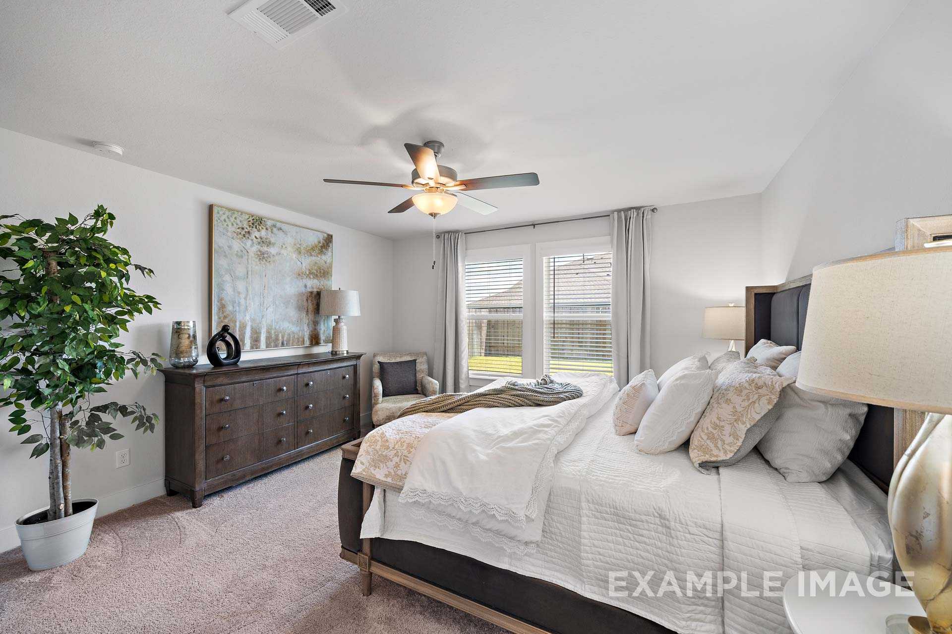 Spacious master bedroom in The Rose B featuring king bed, wooden dresser, potted plant, ceiling fan, and large curtained windows