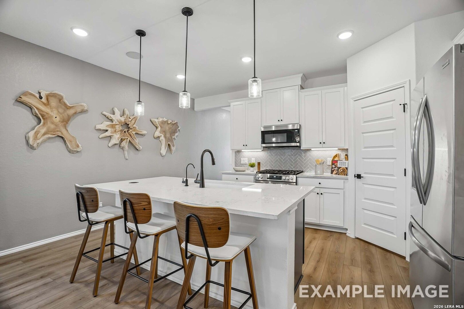 White kitchen with quartz island, pendant lights, stainless appliances, and wood barstools in The Pinecrest E, Converse, Texas