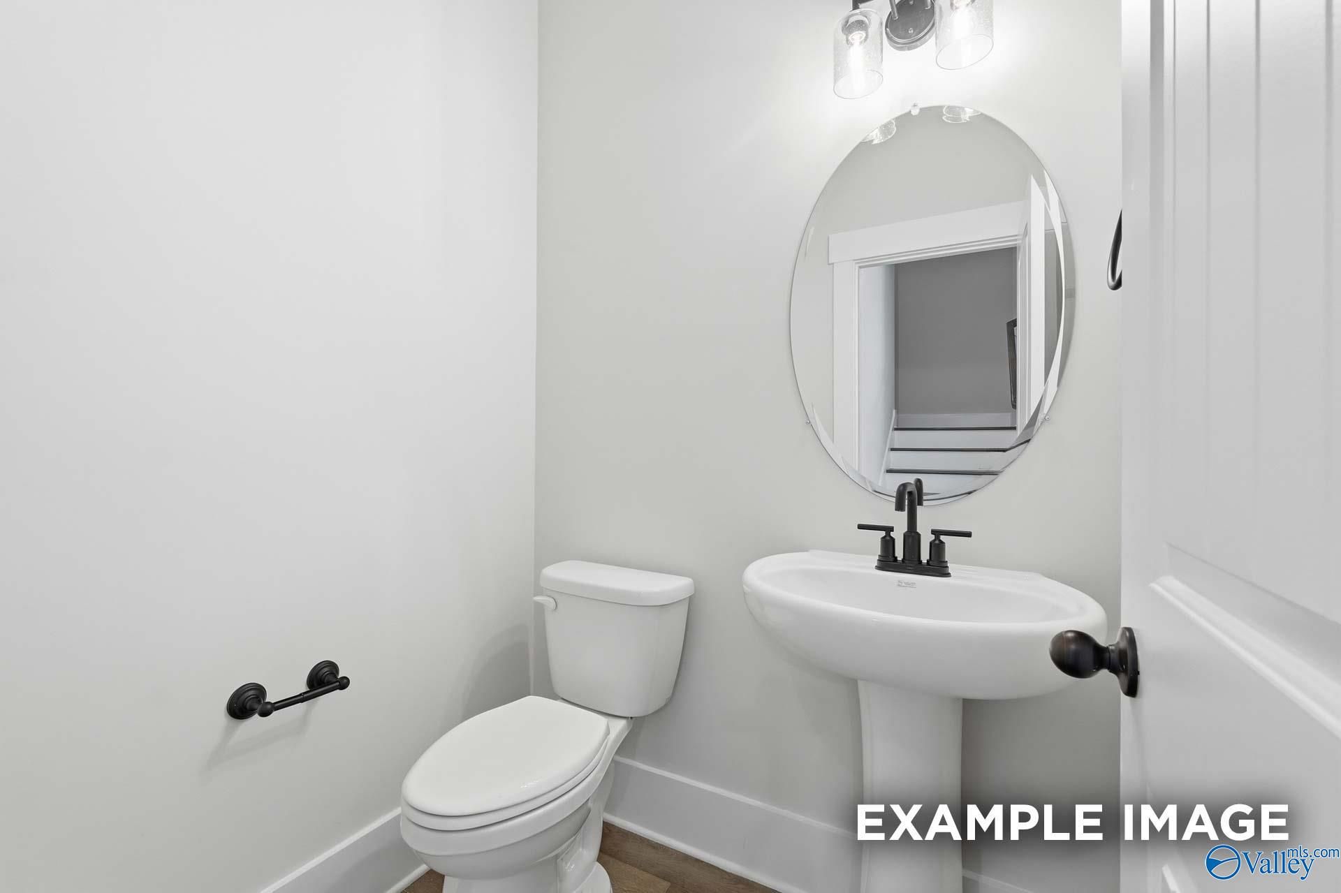 Half bathroom with pedestal sink, oval mirror, and modern black fixtures in The Rockford floor plan, Briercreek homes.