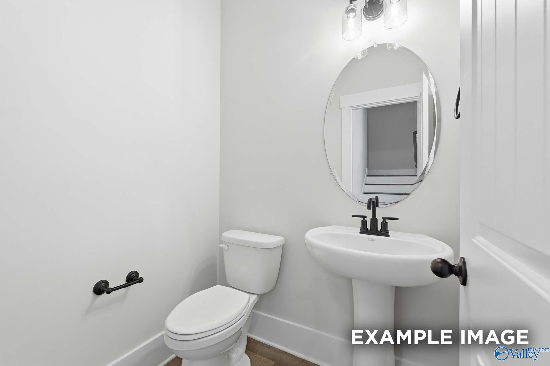 Half bathroom with pedestal sink, oval mirror, and modern black fixtures in The Rockford floor plan, Briercreek homes.