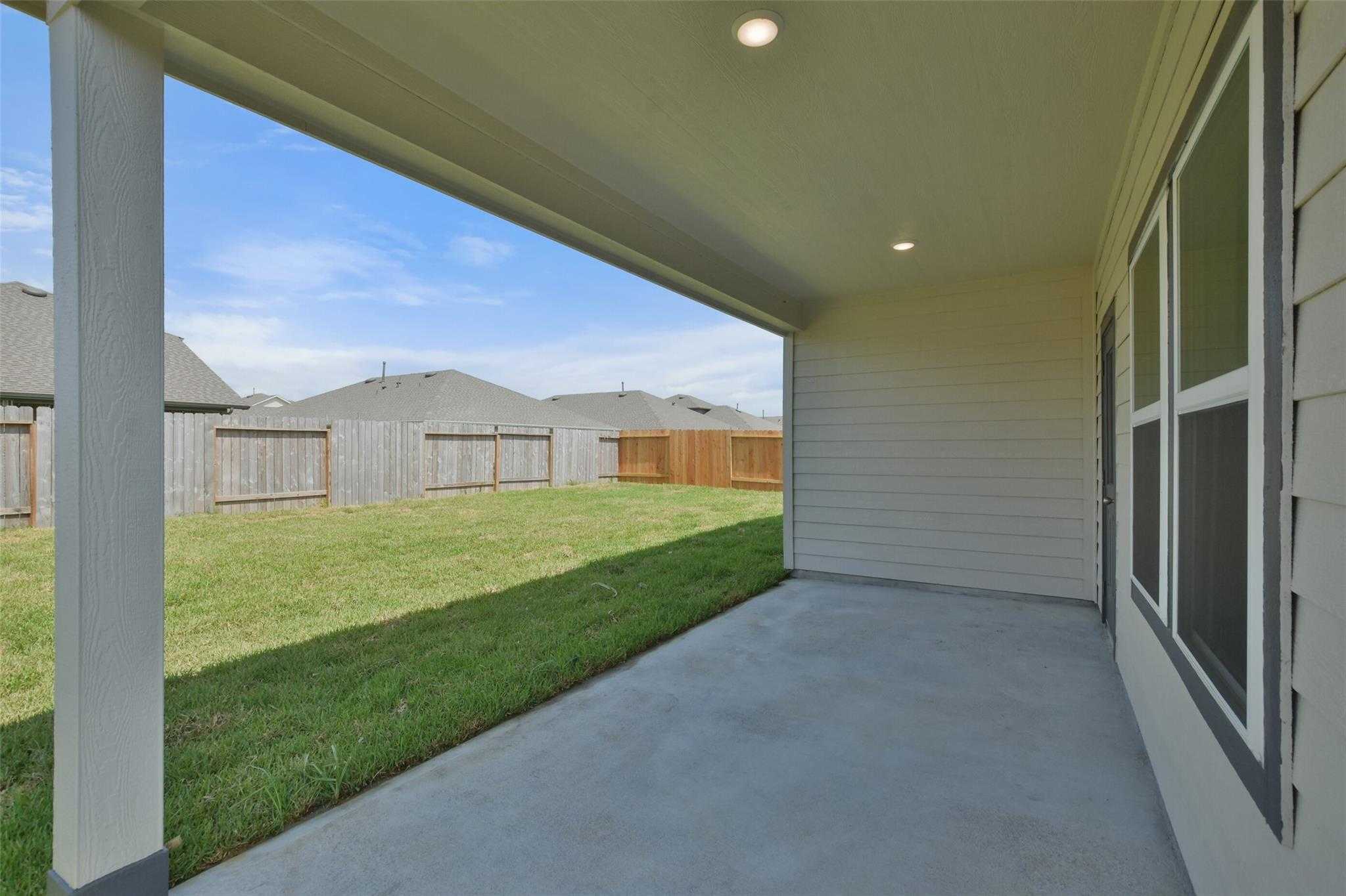 Covered patio with concrete flooring, lush green lawn, and wooden fences in Davidson Homes The Tierra A, River Ranch Meadows, Dayton, Texas