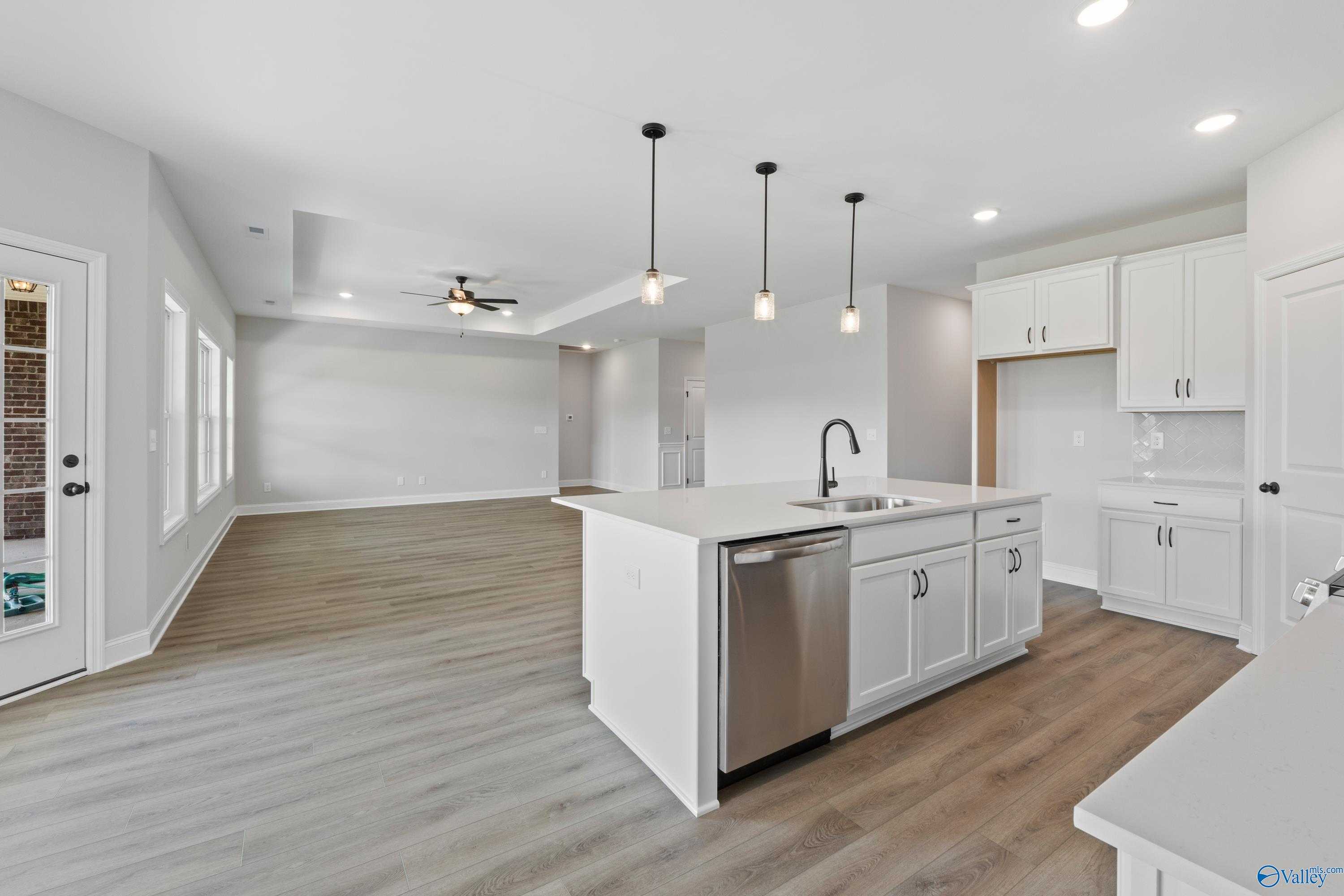 Modern open kitchen with white cabinets, quartz island sink, stainless dishwasher, and wood floors in The Rockford floor plan, Toney AL