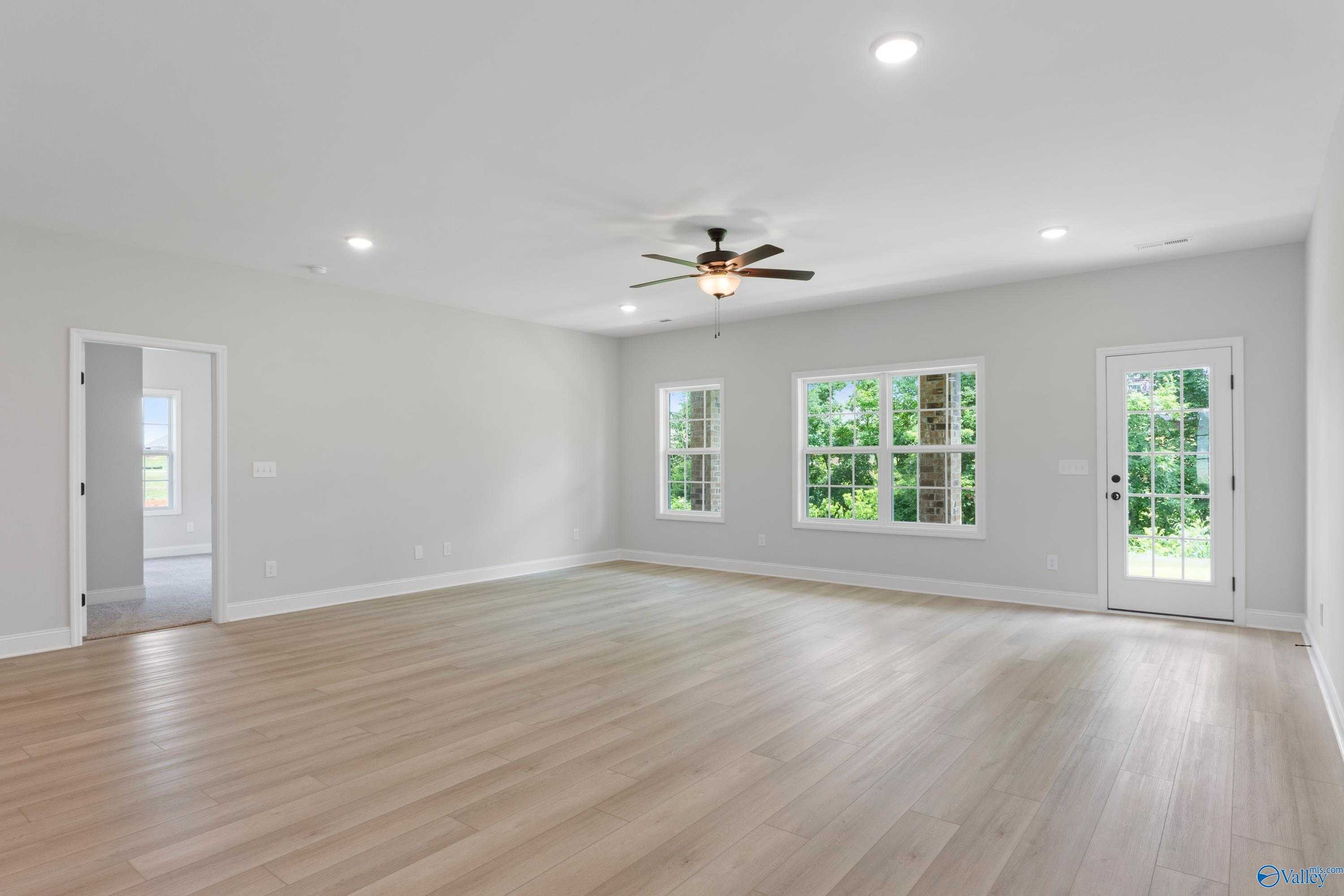 Bright living room with hardwood floors, large windows overlooking trees, ceiling fan in 3-bedroom Davidson Homes The Kirkland, Harvest, AL