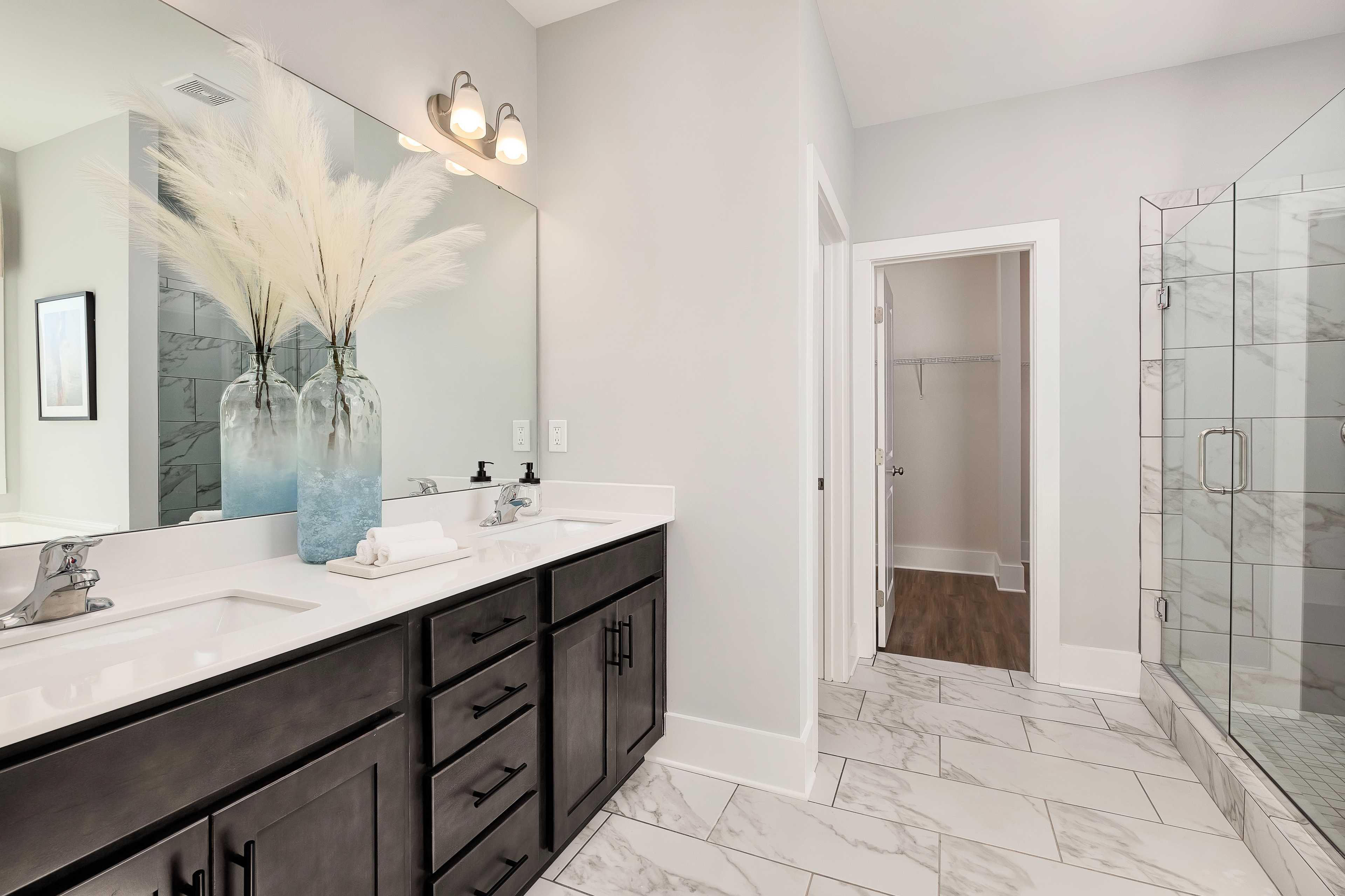 Spacious primary bathroom at Mallard Landing in Athens AL with double dark vanity, glass shower, and walk-in closet
