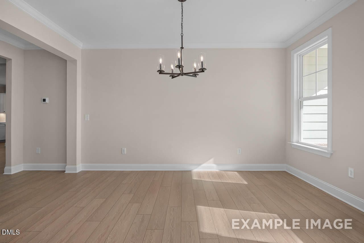 Bright empty dining room with hardwood floors, beige walls, modern chandelier, and large sunny window in Davidson Homes The Crawford D, Angier NC
