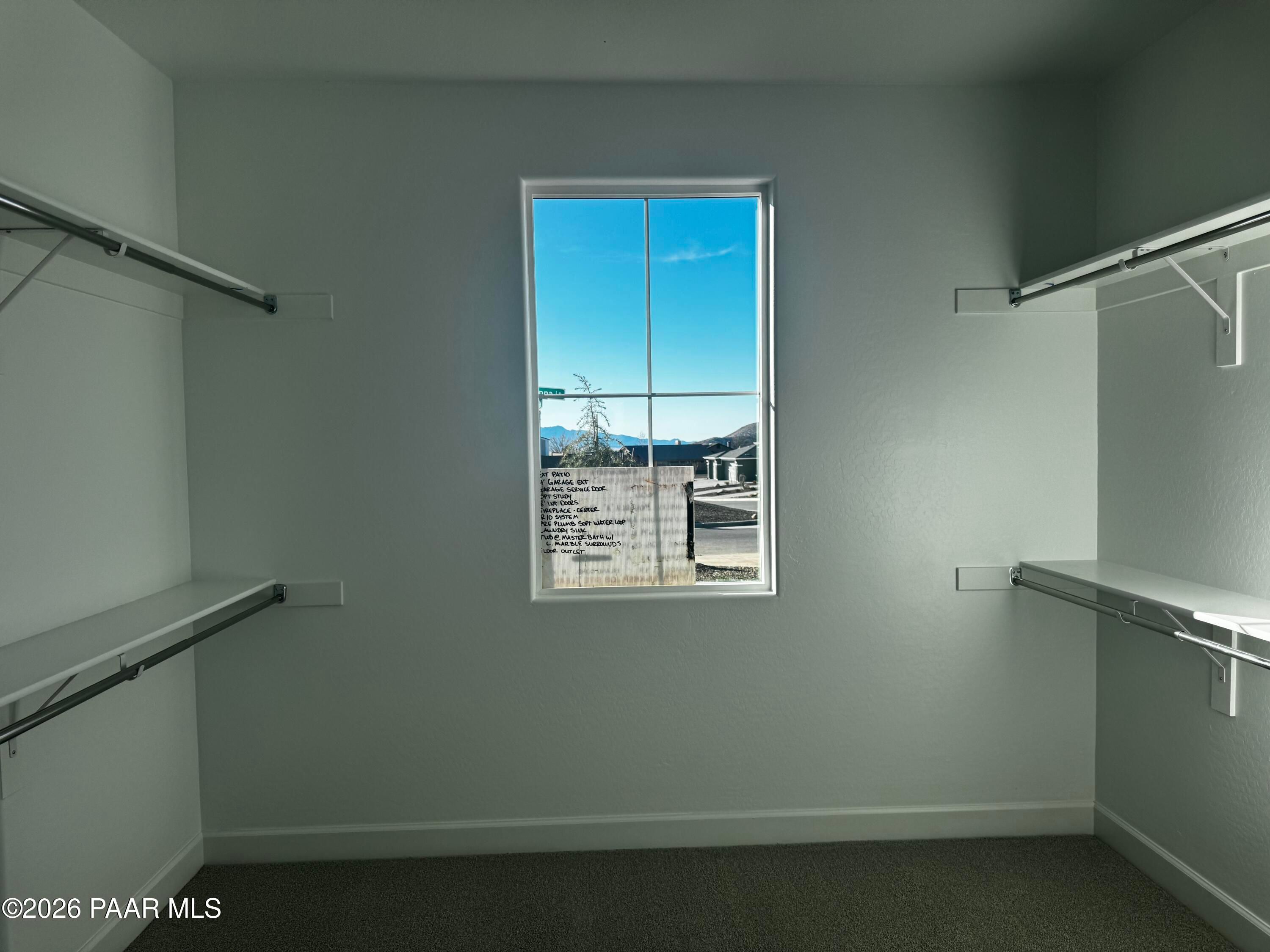 Spacious walk-in closet with white shelves, hanging rods, and large window overlooking Prescott Valley landscape in Evermore Homes The Monarch B