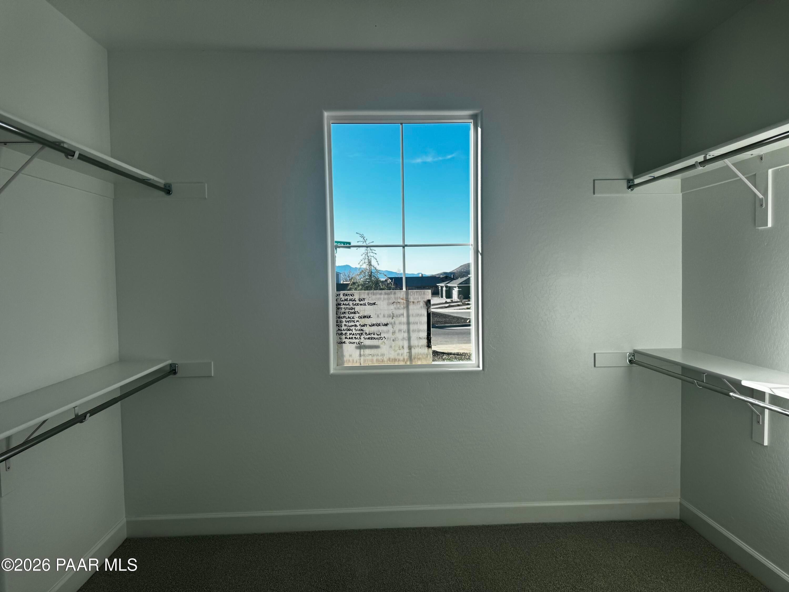 Spacious walk-in closet with white shelves, hanging rods, and large window overlooking Prescott Valley landscape in Evermore Homes The Monarch B