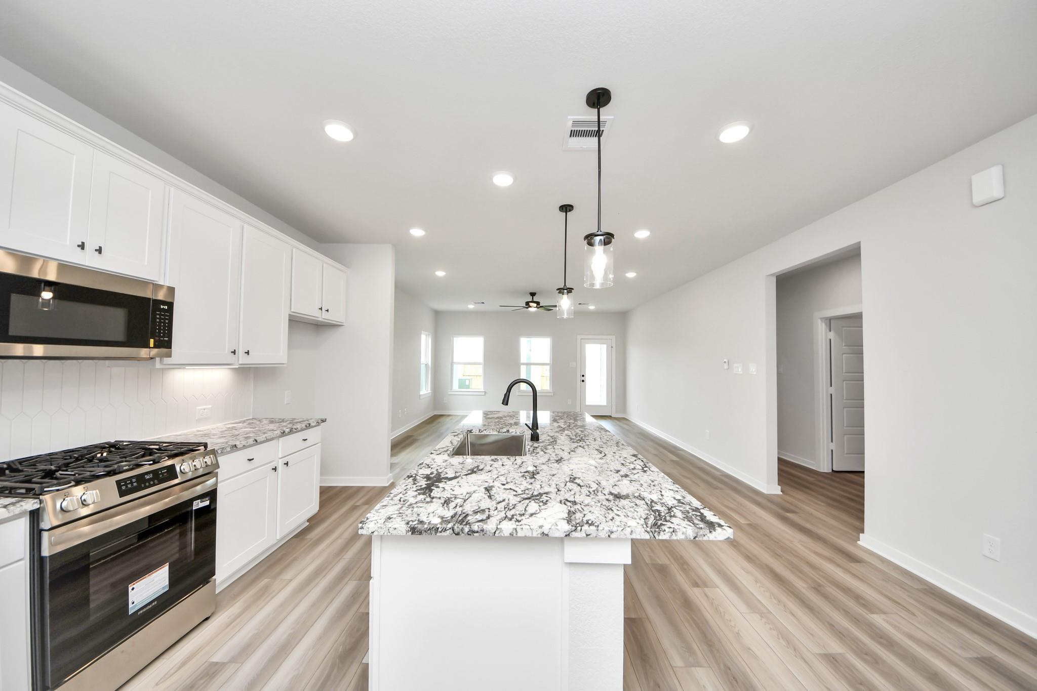 Modern kitchen with granite island and white cabinets in The Sorrento E floor plan at Sundance Cove in Crosby, Texas.
