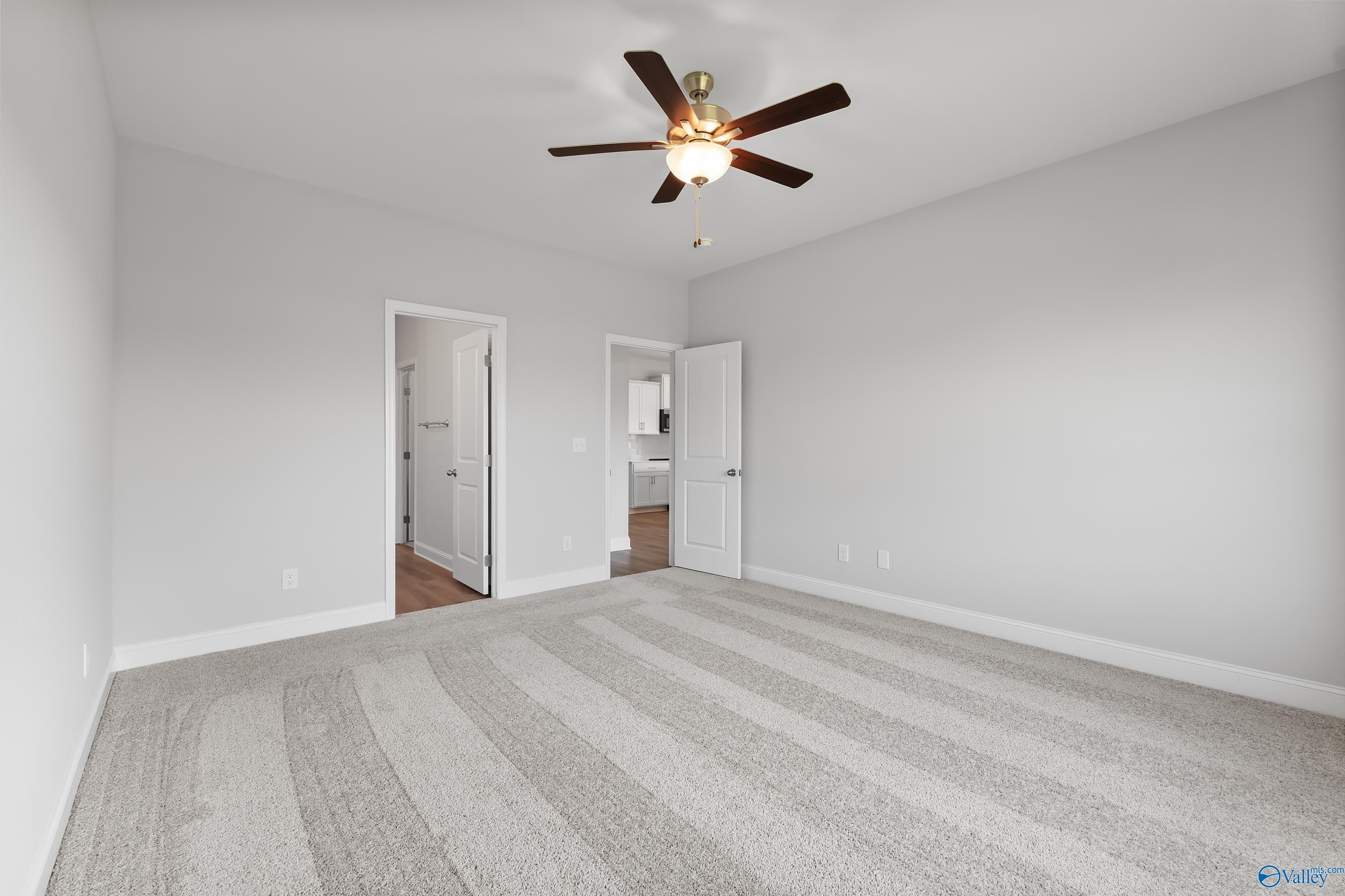 Spacious bedroom with ceiling fan, gray carpet, and doors to bathroom in Davidson Homes The Daphne, Hazel Green, AL