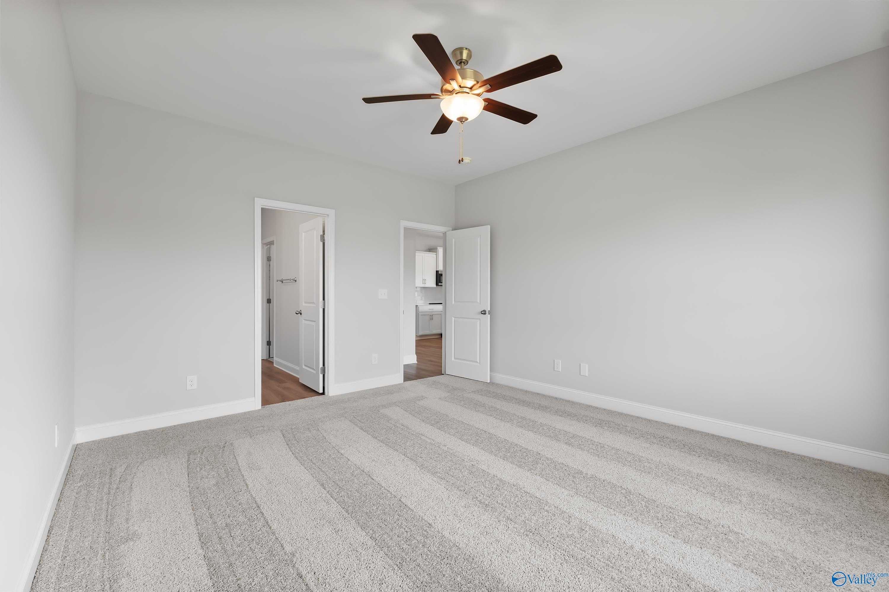 Spacious bedroom with ceiling fan, gray carpet, and doors to bathroom in Davidson Homes The Daphne, Hazel Green, AL