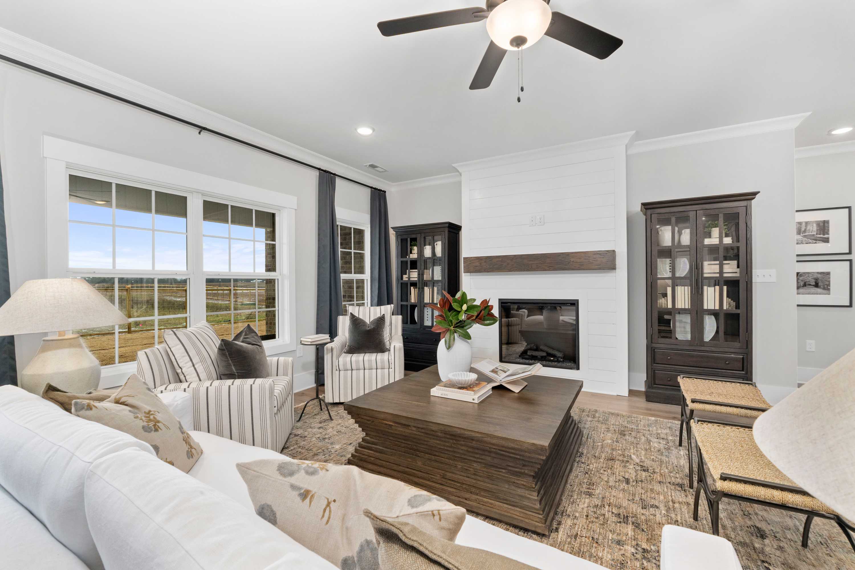 Spacious living room at Kendall Farms in Toney Alabama with shiplap fireplace, large field-view windows, and plush neutral seating