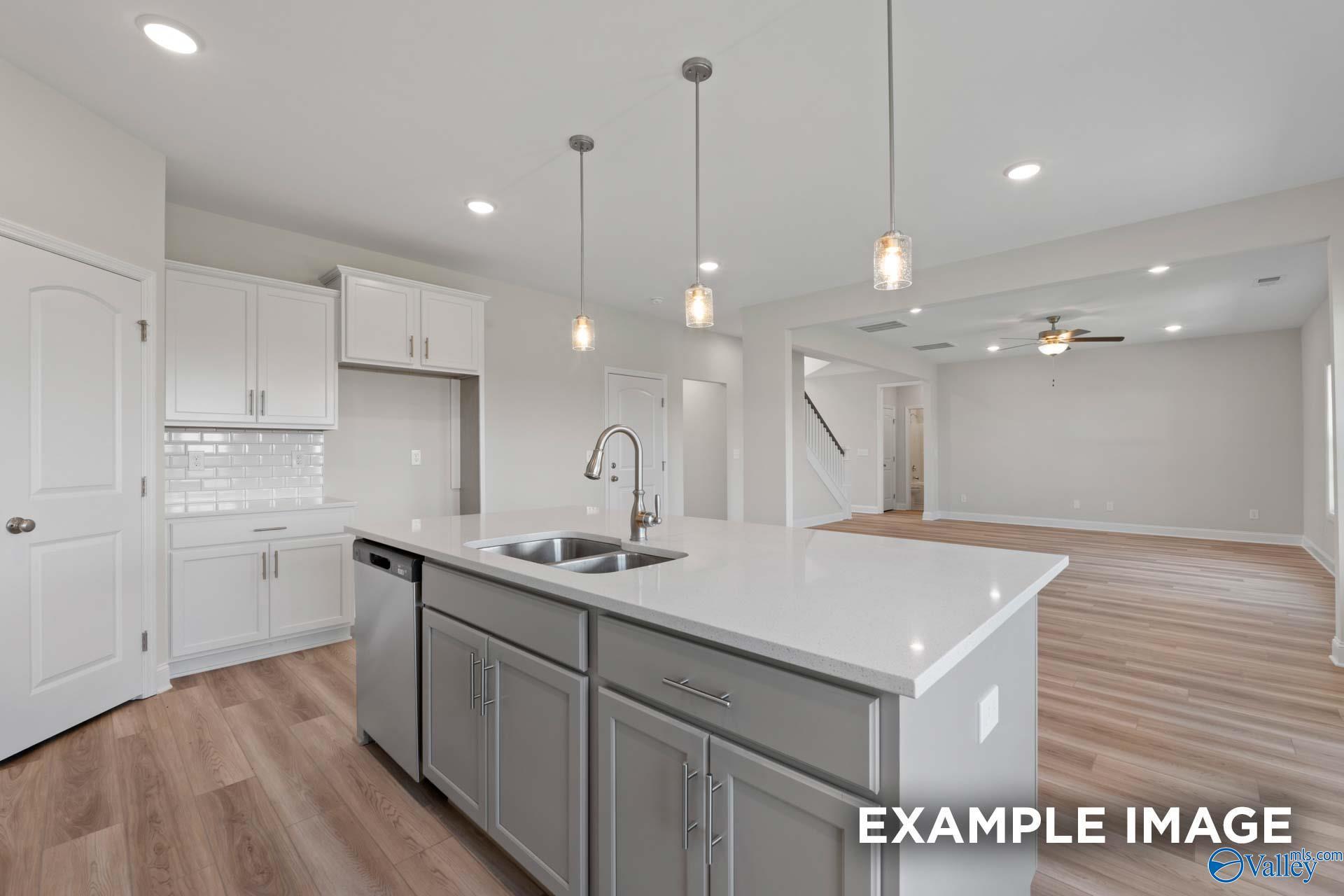 Open-concept kitchen with white cabinets, subway tile backsplash, quartz island, and pendant lights in The Madison A by Davidson Homes, Toney, AL