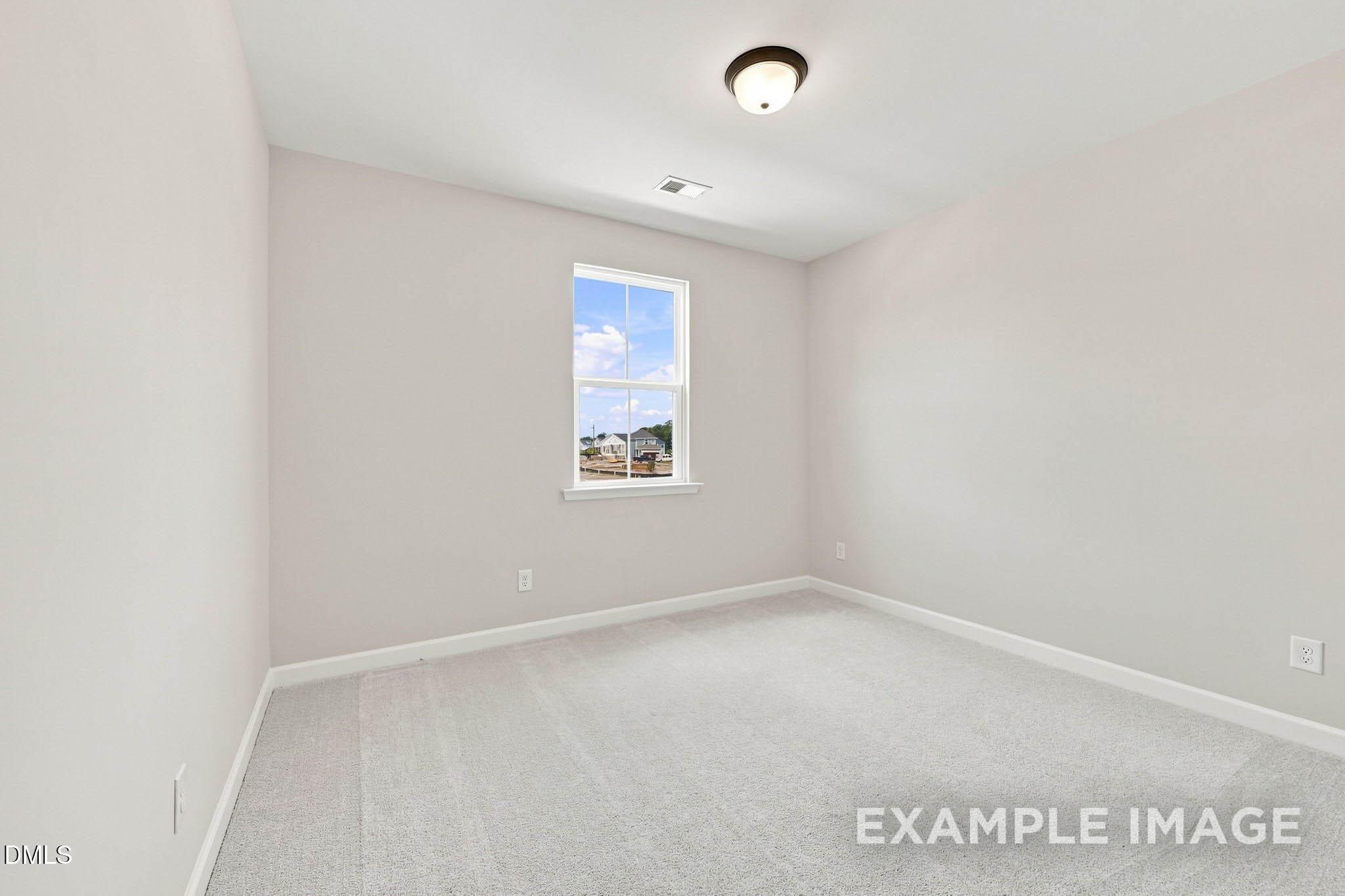 Bright empty bedroom with plush carpet, white walls, and window in Davidson Homes The Harris A plan, Knightdale, NC