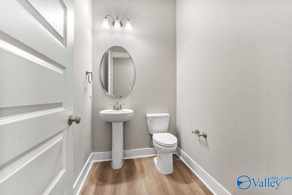 Elegant powder room with pedestal sink, oval mirror, and white toilet in Evermore Homes The Oxford, Owens Cross Roads, Alabama