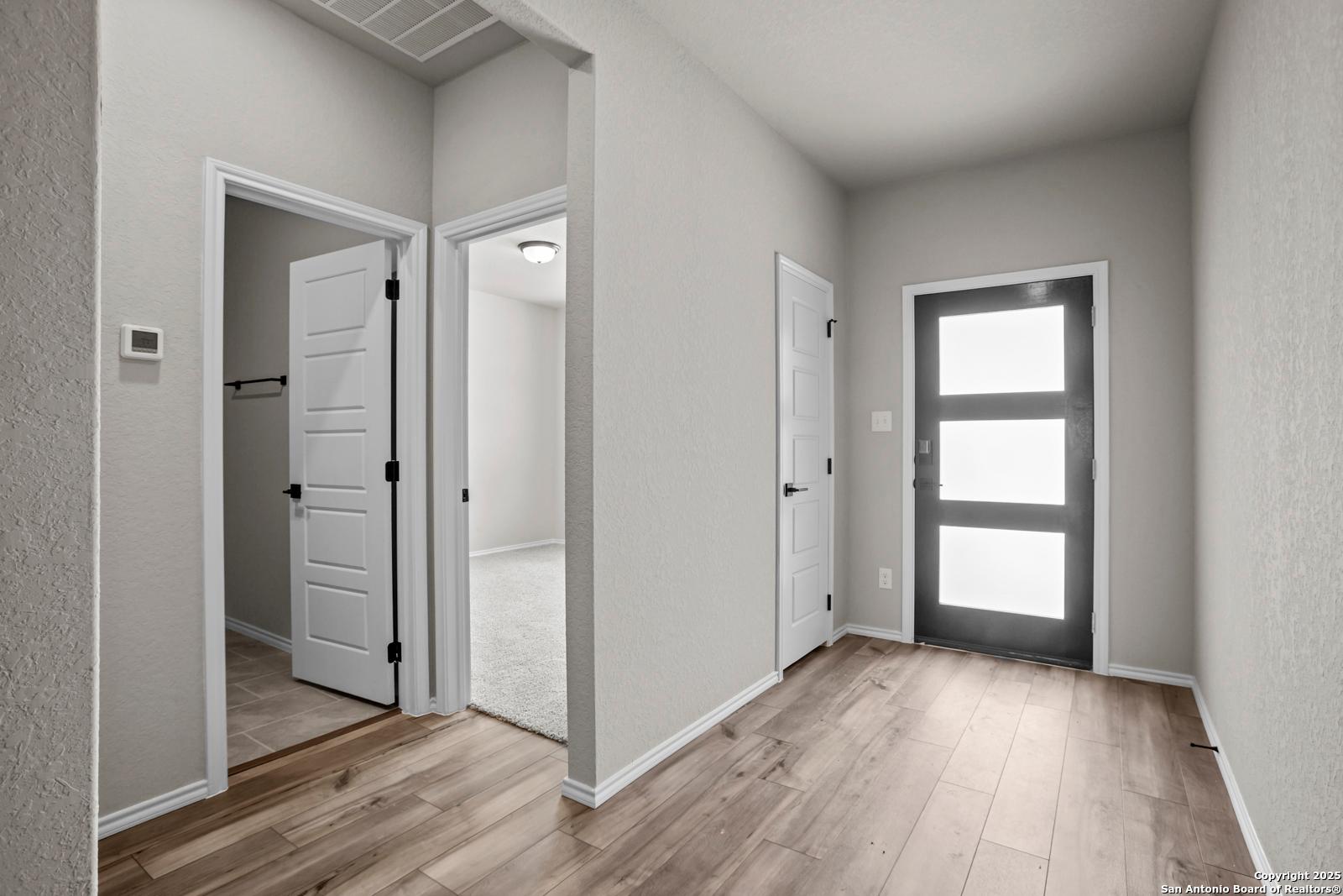 Modern entryway hallway with hardwood floors, white doors, and frosted glass front door in Davidson Homes The Daphne G, San Antonio