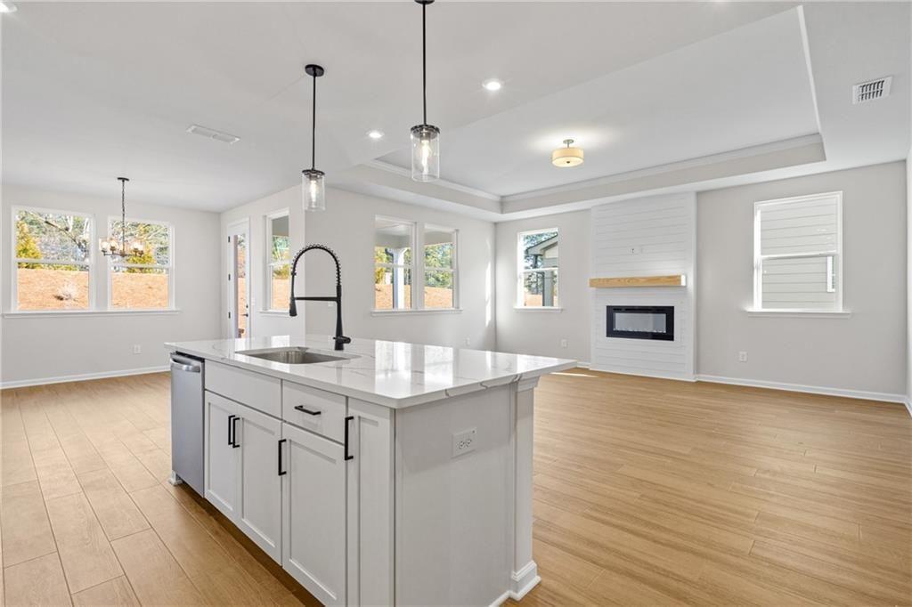 Modern open-concept kitchen with white island, stainless dishwasher, pendant lights, and gas fireplace in The Edison A, Loganville, GA
