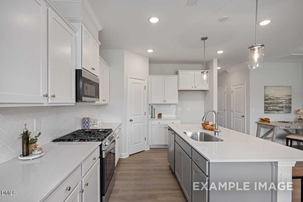 Modern kitchen featuring white shaker cabinets, stainless appliances, granite island, and subway tile backsplash in Davidson Homes The Warren, Fuquay-Varina, NC