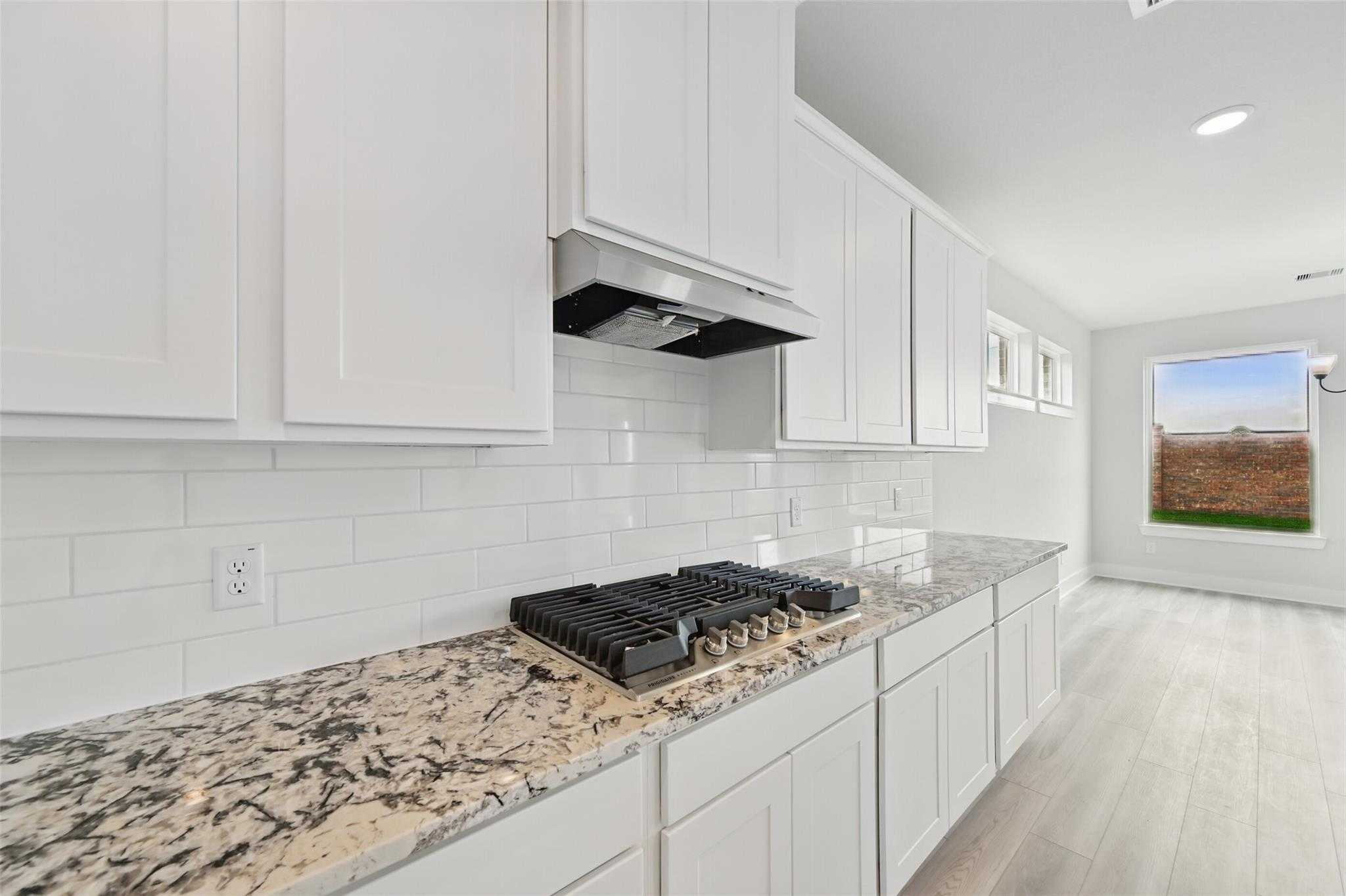 Modern white kitchen with granite countertops, subway tile backsplash, gas cooktop in Davidson Homes The Victoria C, Lago Mar, Texas City