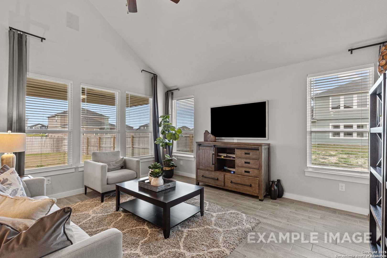 Bright living room with vaulted ceiling, large windows, wooden media console and cozy gray sofa in Davidson Homes Collin B, Seguin Texas