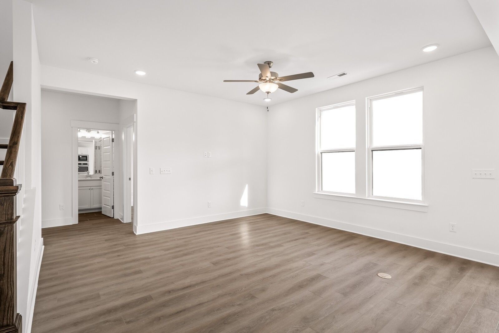 Bright living room with hardwood floors, large windows, ceiling fan, staircase, and powder room in The Willow D home, Mt. Juliet, TN