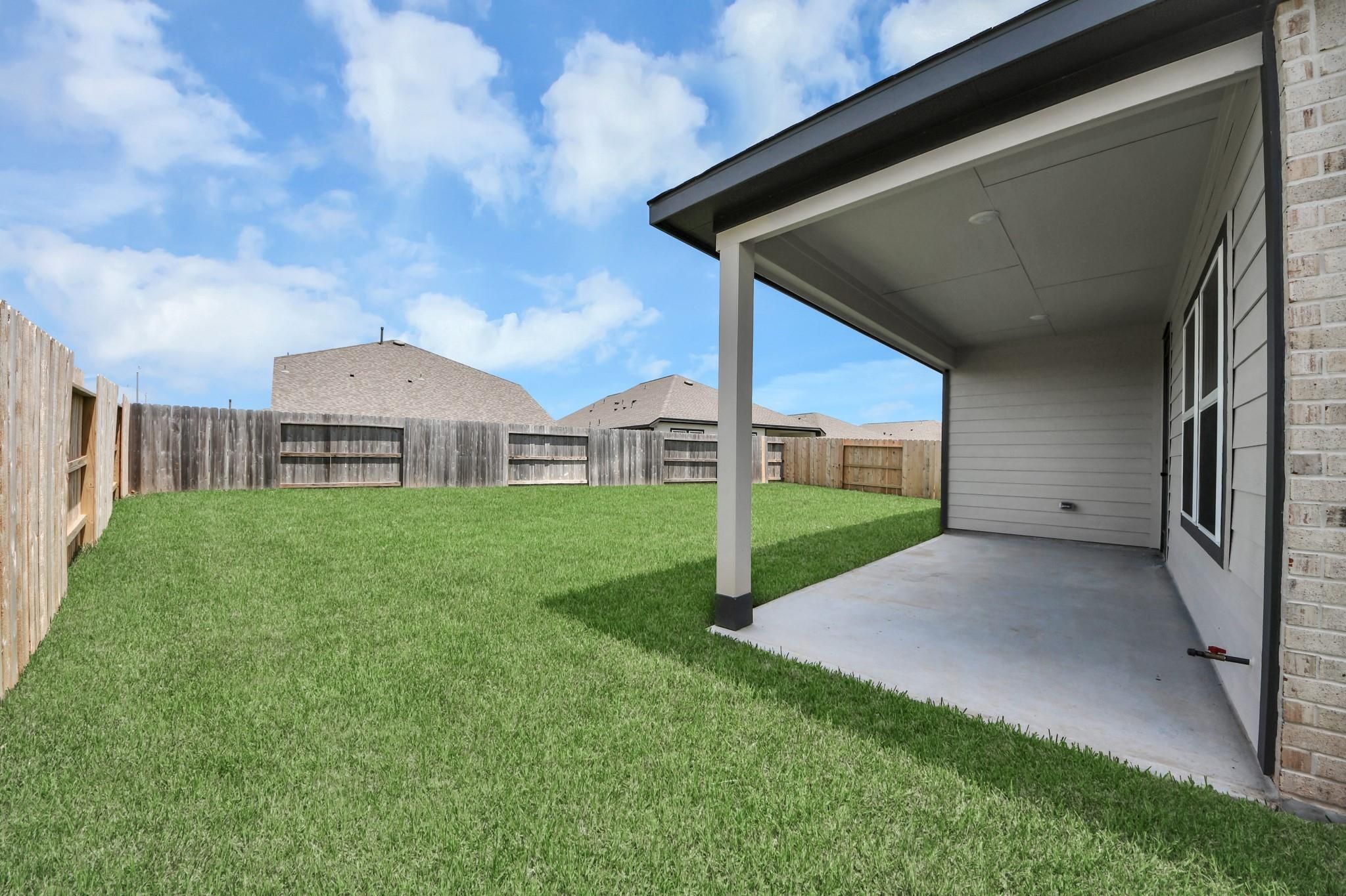 Covered concrete patio overlooking spacious fenced backyard with lush green lawn at Davidson Homes The Laguna C in Sunterra, Katy, Texas