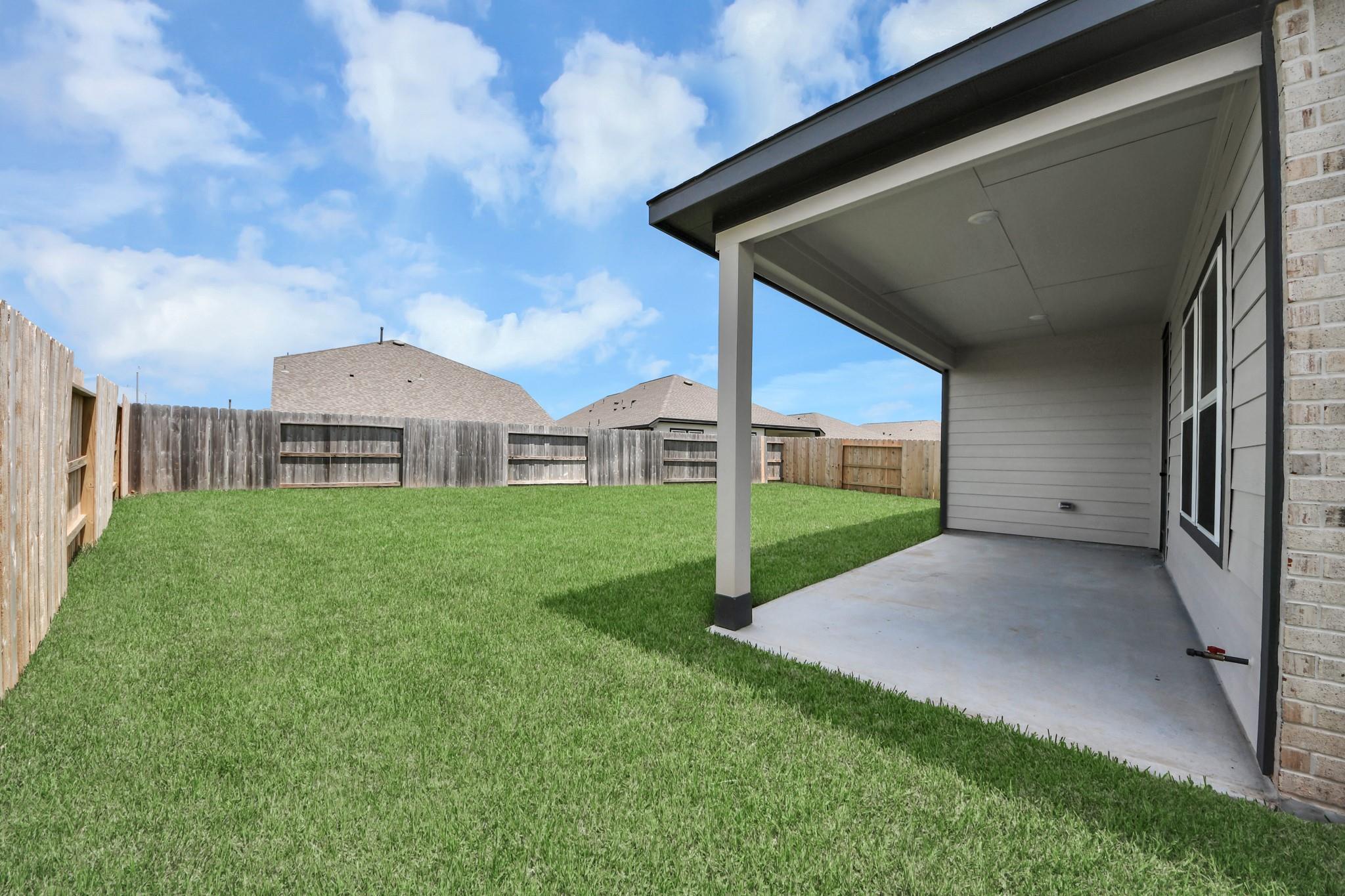 Covered concrete patio overlooking spacious fenced backyard with lush green lawn at Davidson Homes The Laguna C in Sunterra, Katy, Texas