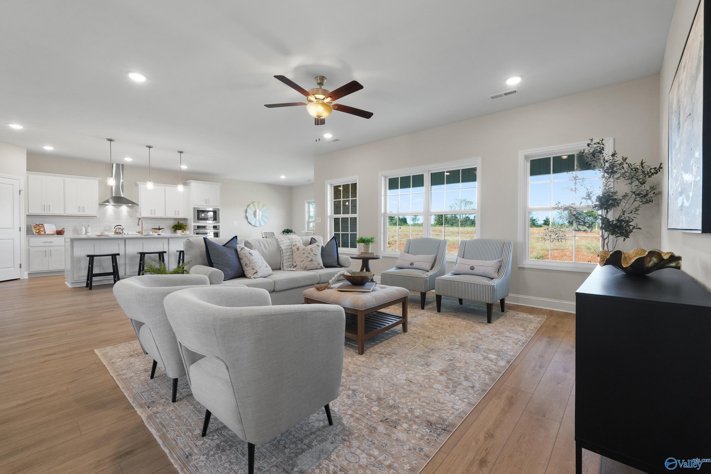 Open living room with gray sectional sofa, chairs, and ceiling fan overlooking greenery in Davidson Homes The Rockford B, Toney, AL