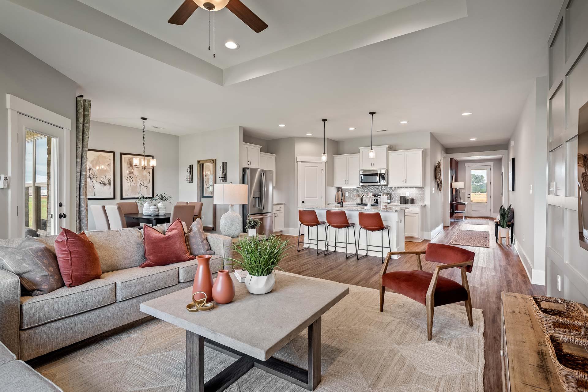 Spacious open-concept living room at Heritage Lakes in New Market Alabama with gray sectional sofa, red accents, kitchen island, hardwood floors