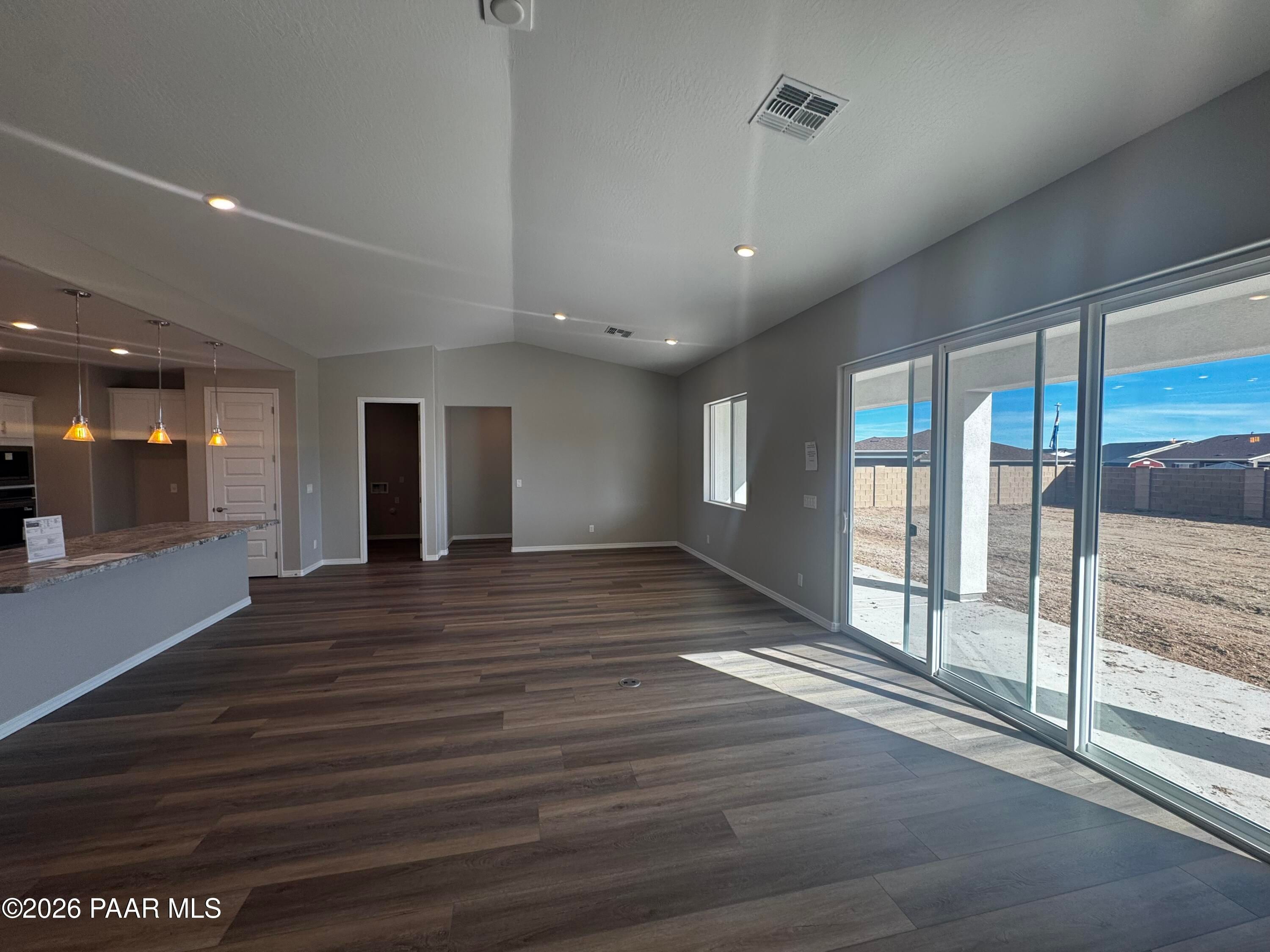 Spacious open great room with wood laminate floors, kitchen peninsula, and large sliding doors to desert backyard in Daybreak B home, Prescott AZ