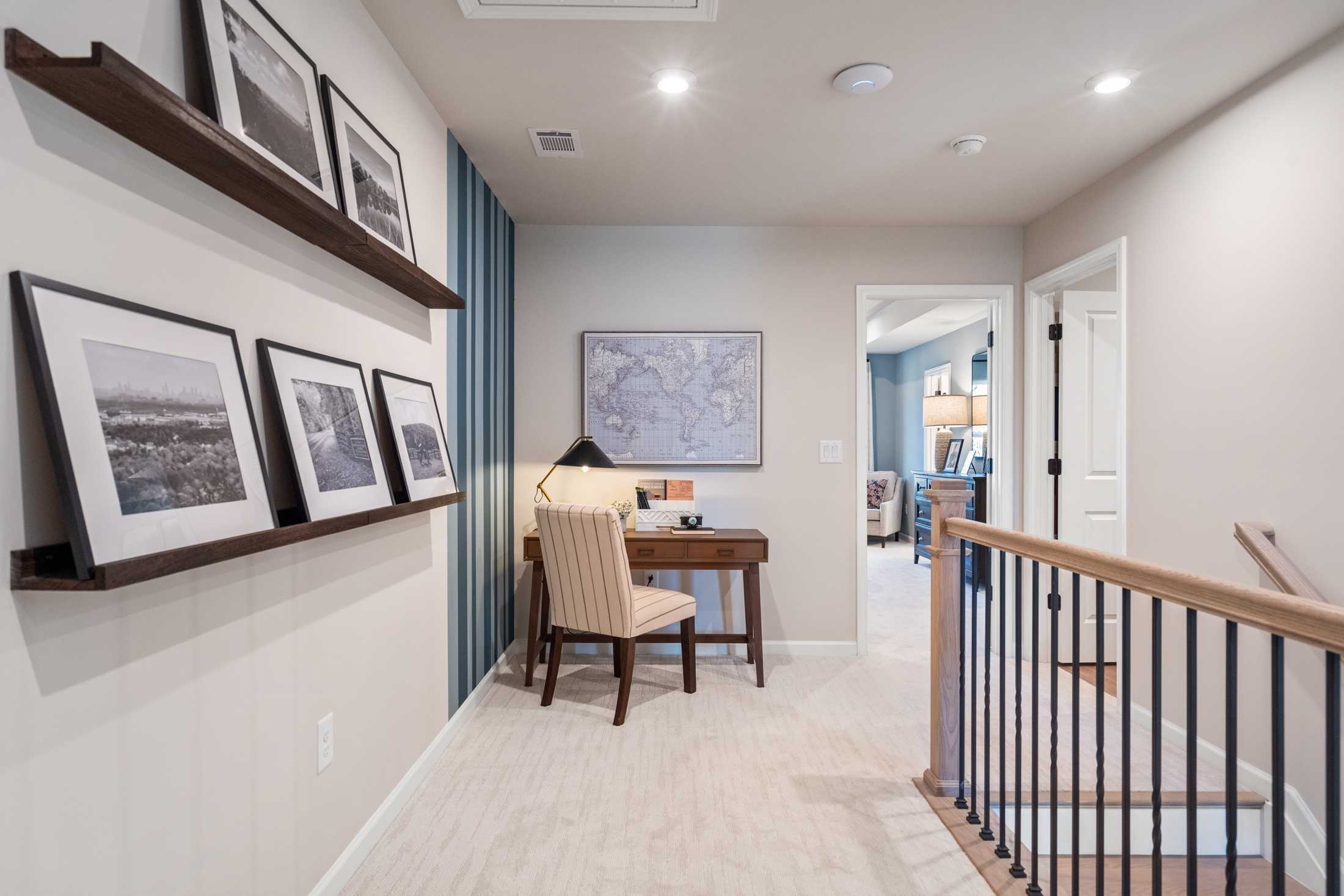 Upper floor study nook in The Marion A home featuring desk, armchair, world map, and framed photos
