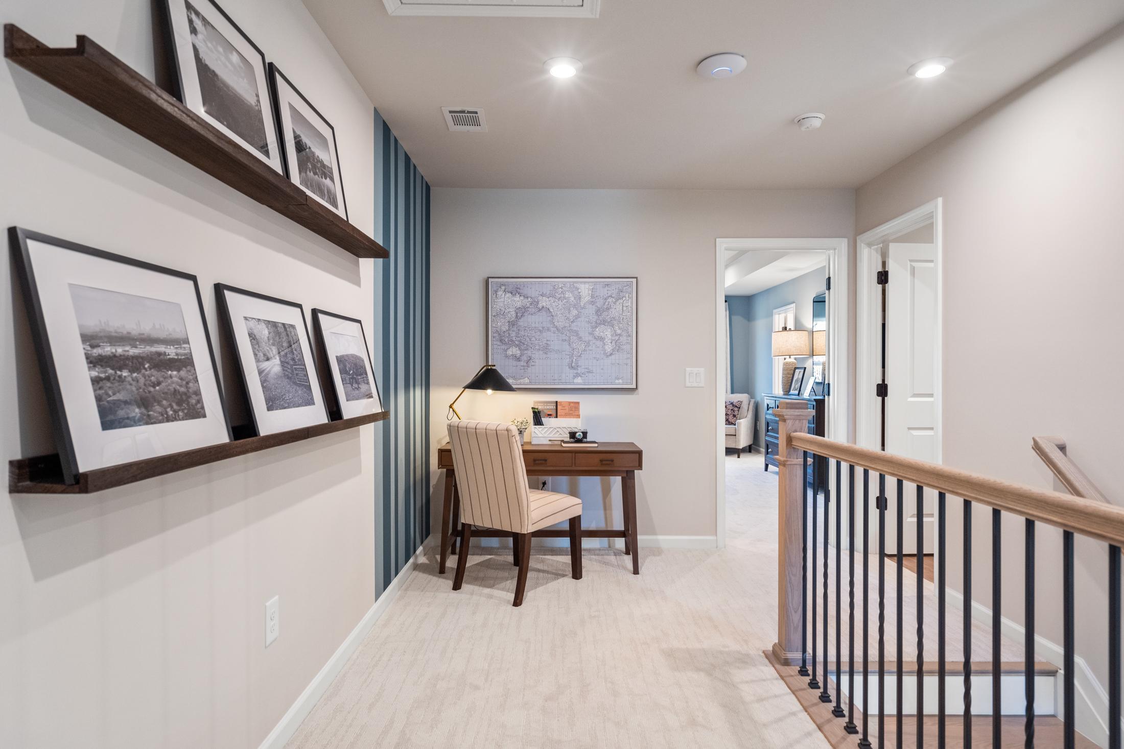 Upper floor study nook in The Marion A home featuring desk, armchair, world map, and framed photos