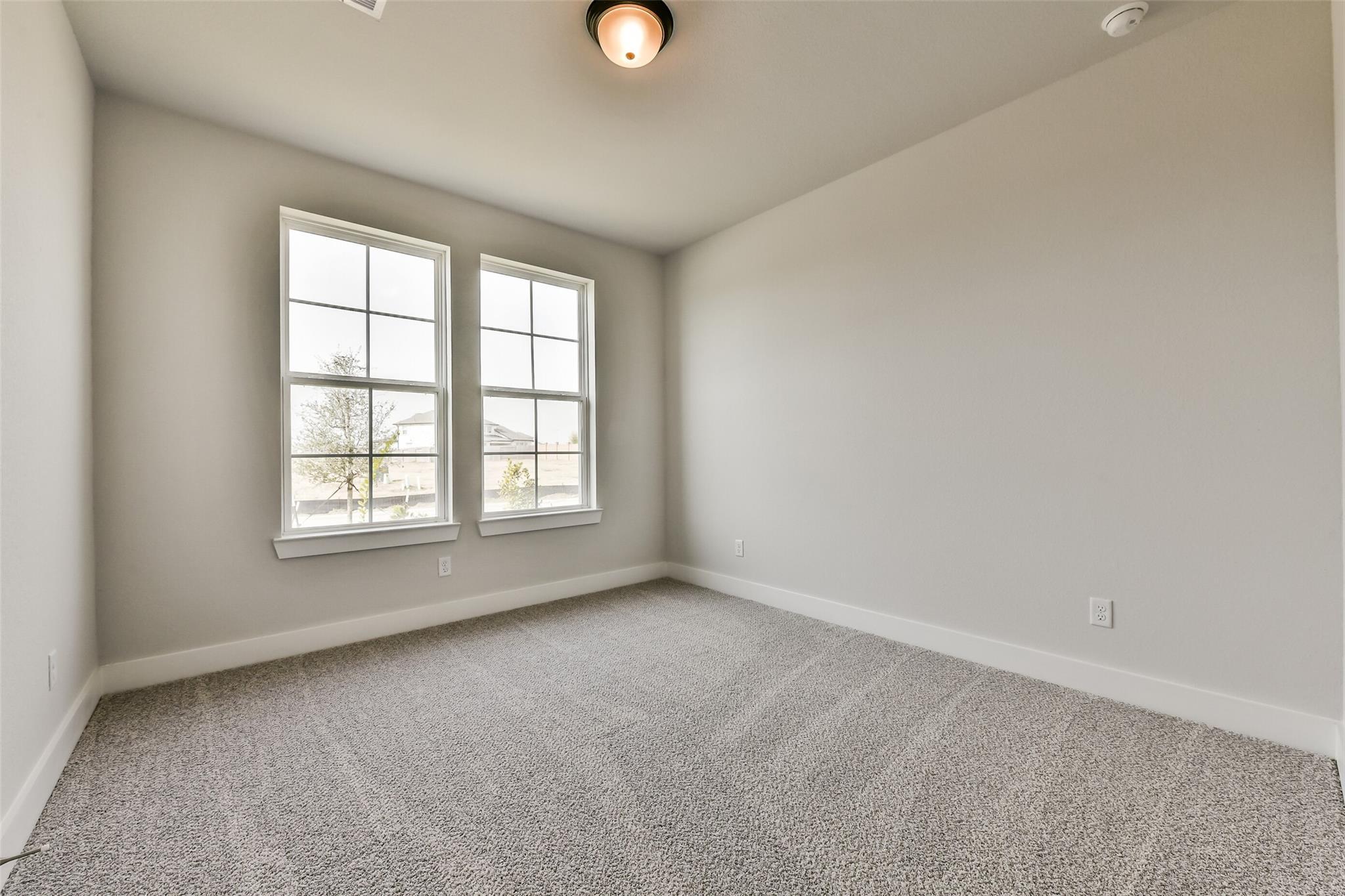 Bright empty bedroom with beige carpet, light gray walls, and double windows in Davidson Homes The George A, Lago Mar, Texas City